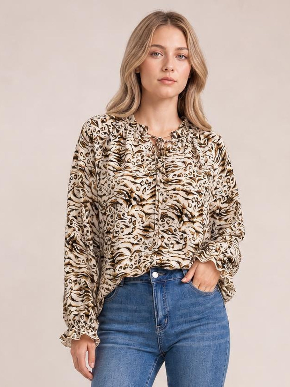 Model wears a long printed blouse with a tie neck, frill trim, and flounce sleeves in a beige, brown, and black animal-inspired pattern.