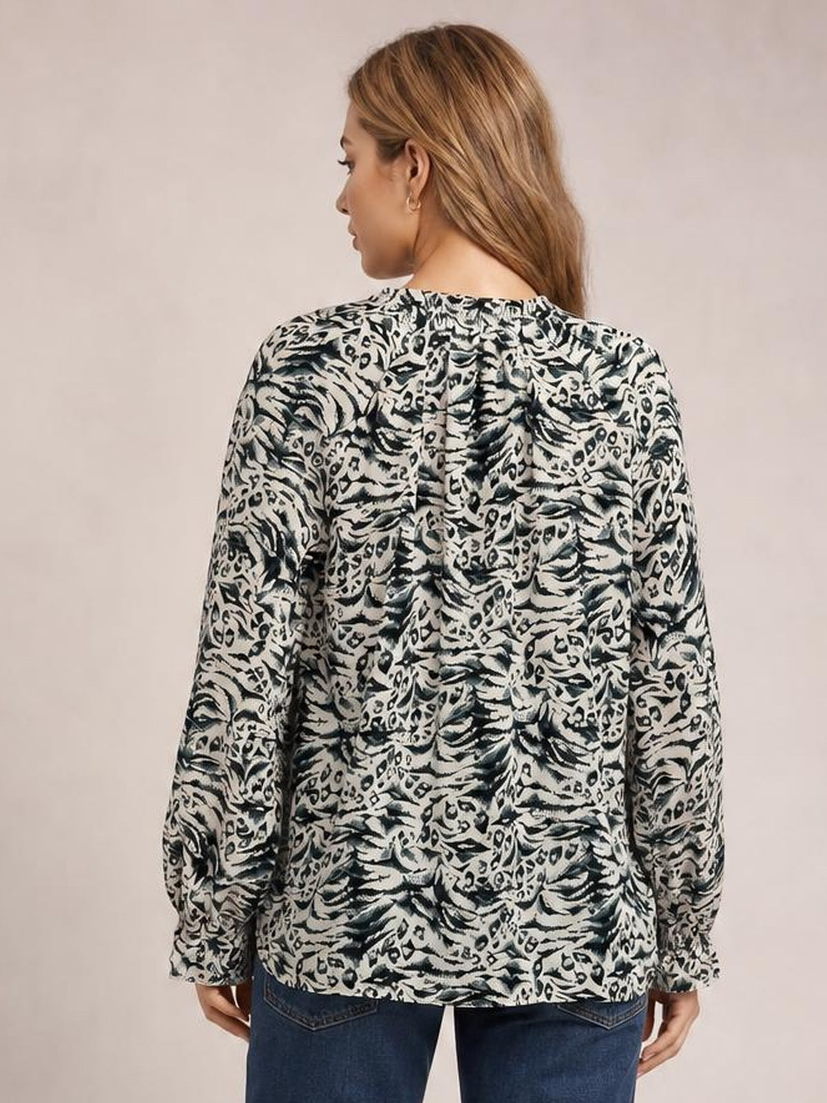 A model stands facing away in a black-and-white printed blouse with long sleeves, a relaxed long silhouette, and a softly gathered neckline.
