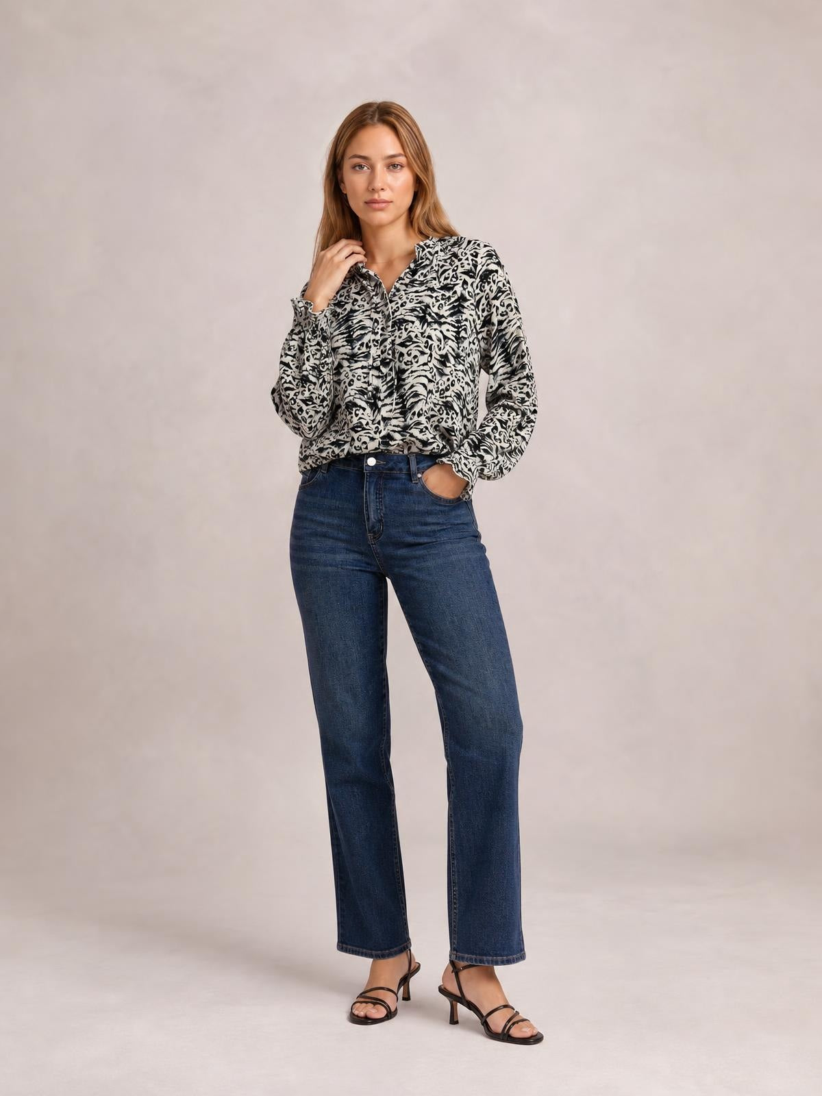 Model wearing a black-and-white printed tie-neck blouse with frill trim and long flounce sleeves, standing with one hand at her neck and one in her pocket.