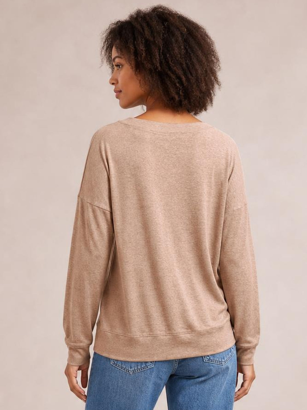 Model shown from behind wearing a beige dropped shoulder blouse with long sleeves, a relaxed silhouette, and a wide banded hem.