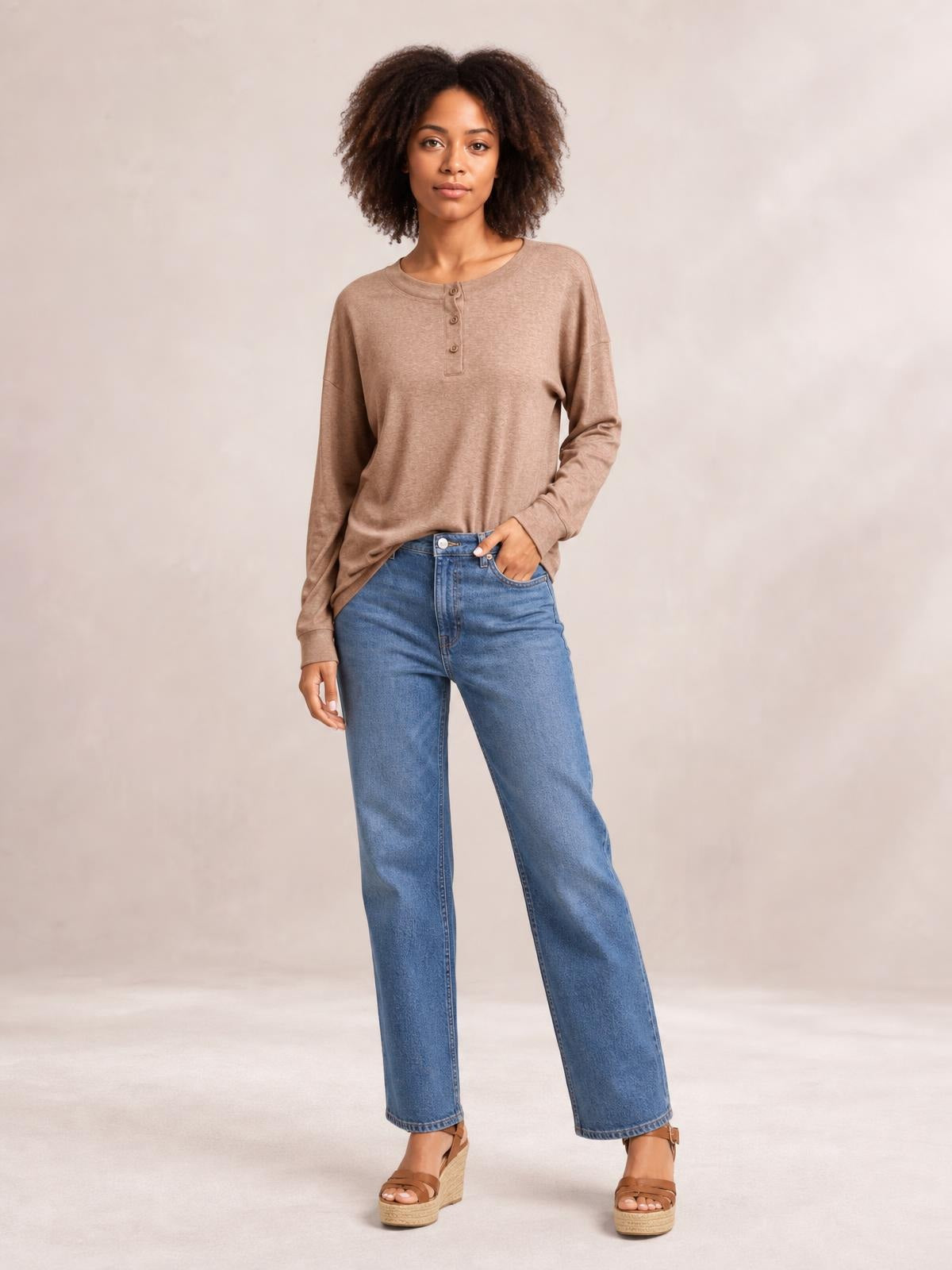 Model wearing a taupe quarter-button blouse with dropped shoulders, long sleeves, and a relaxed silhouette, paired with blue wide-leg jeans.
