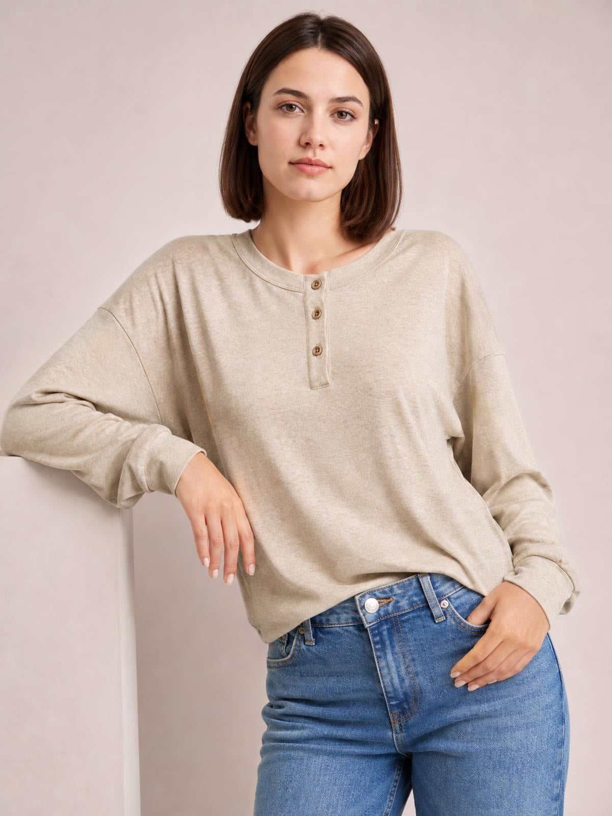 A model poses in a beige quarter-button dropped-shoulder blouse with a relaxed silhouette, long sleeves, and a round neckline.