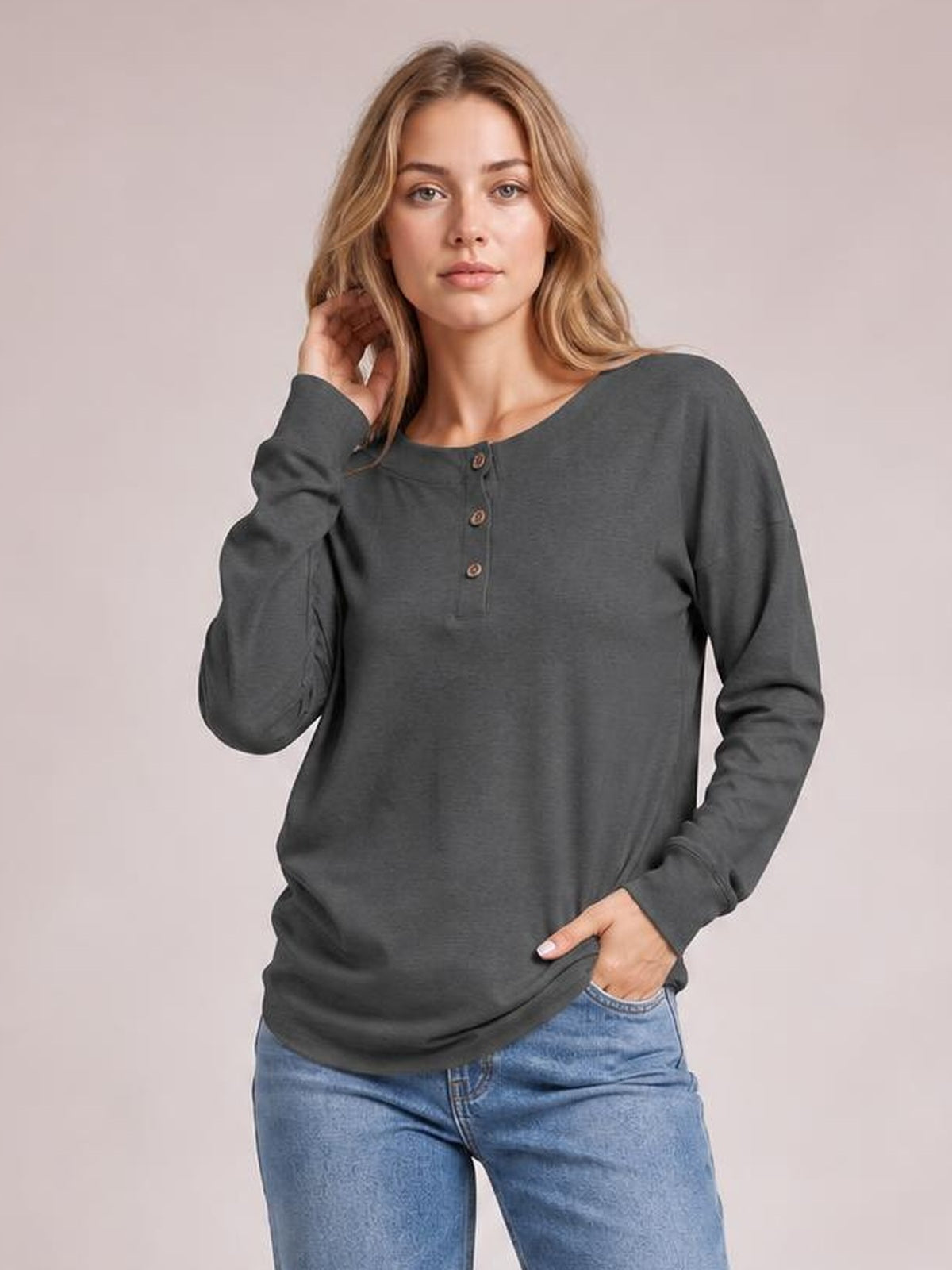 Model wears a charcoal quarter-button dropped shoulder blouse with a relaxed fit, round neckline, long sleeves, and a straight silhouette, posing with one hand in her pocket.