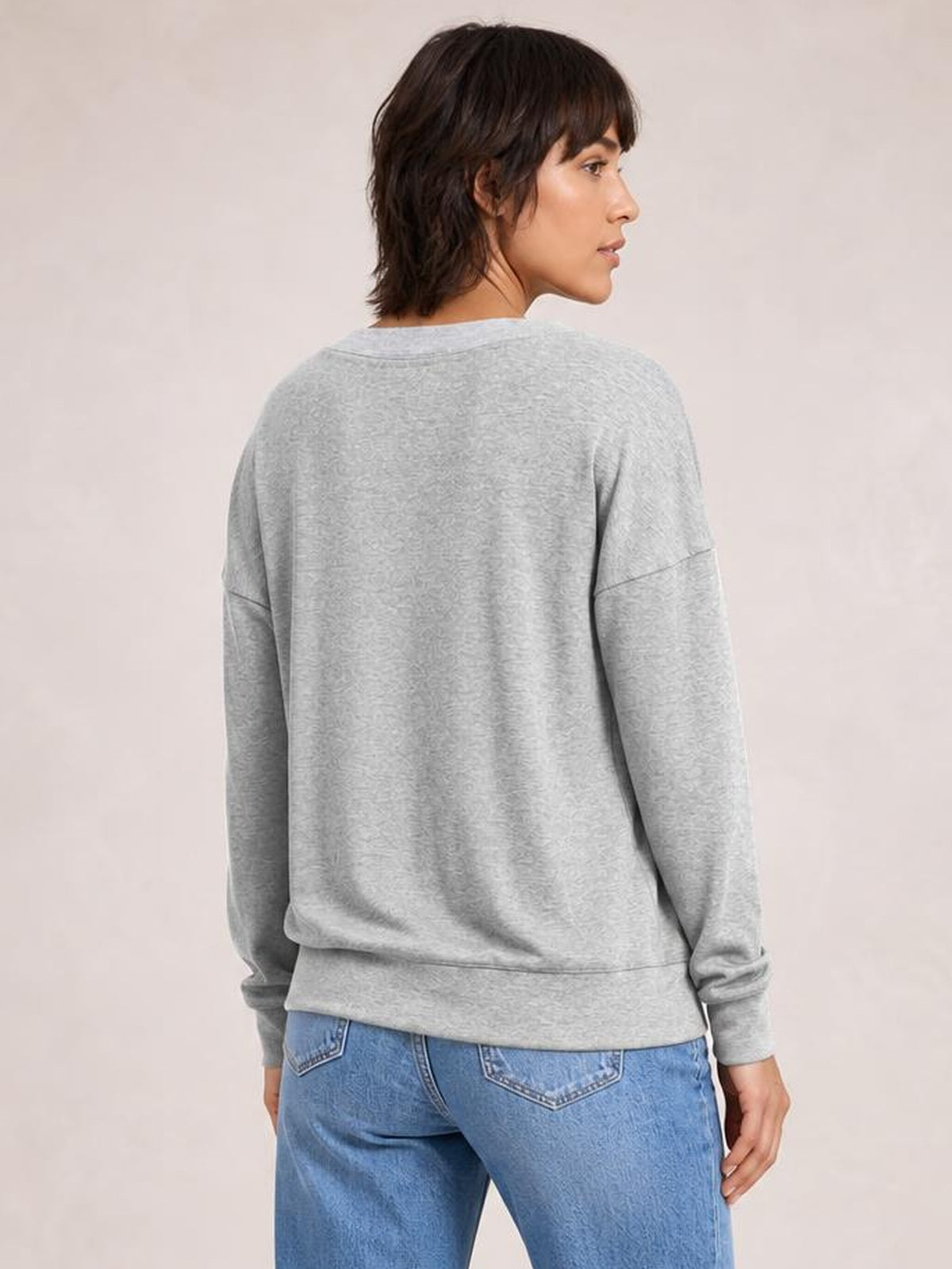 Model shown from the back in a light gray dropped shoulder blouse with long sleeves, relaxed silhouette, seam detailing, and a ribbed hem.