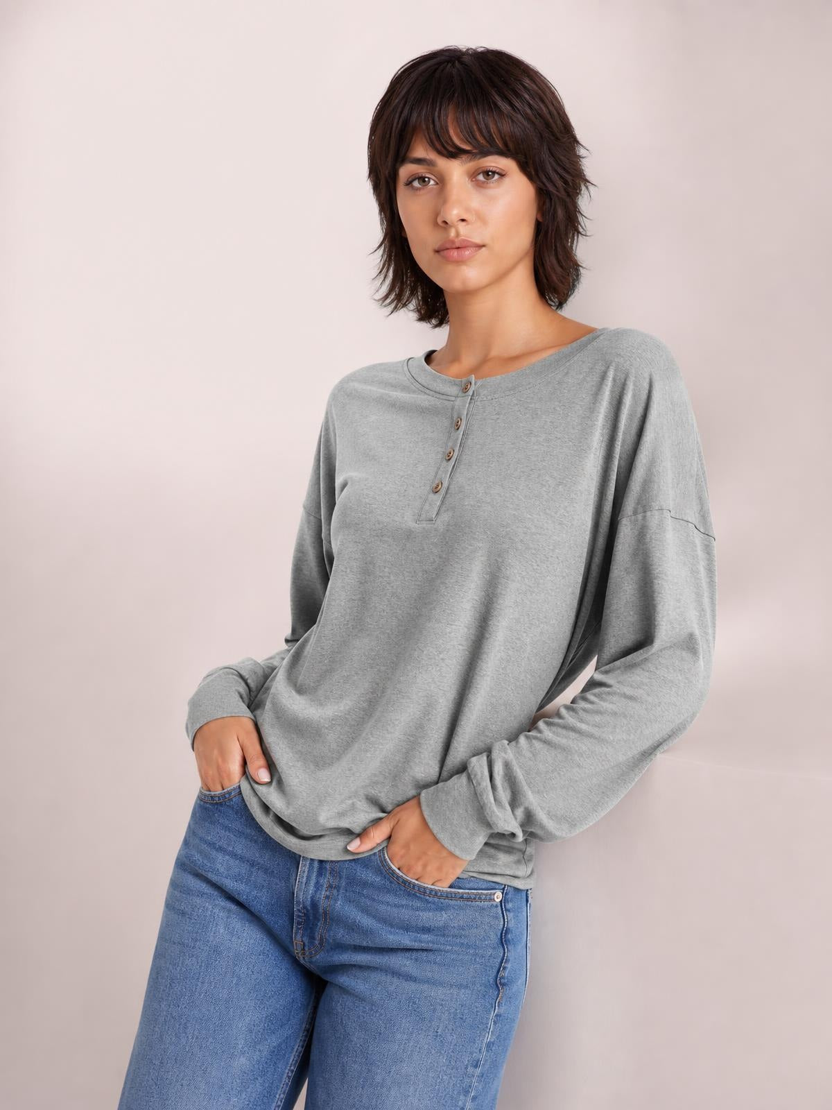 Model poses with hands in her pockets wearing a gray quarter-button dropped shoulder blouse with a relaxed silhouette and long sleeves.