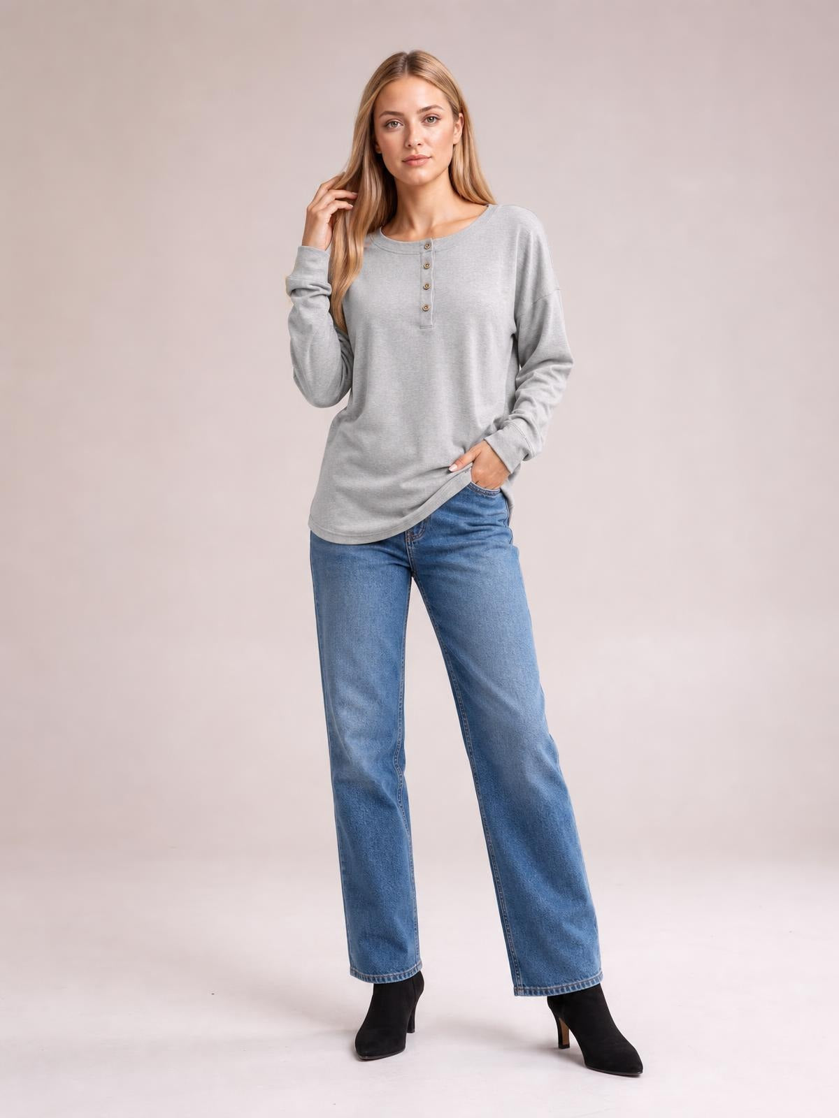 A model wears a gray quarter-button dropped-shoulder blouse with long sleeves and a relaxed silhouette, standing with one hand in her jeans pocket.