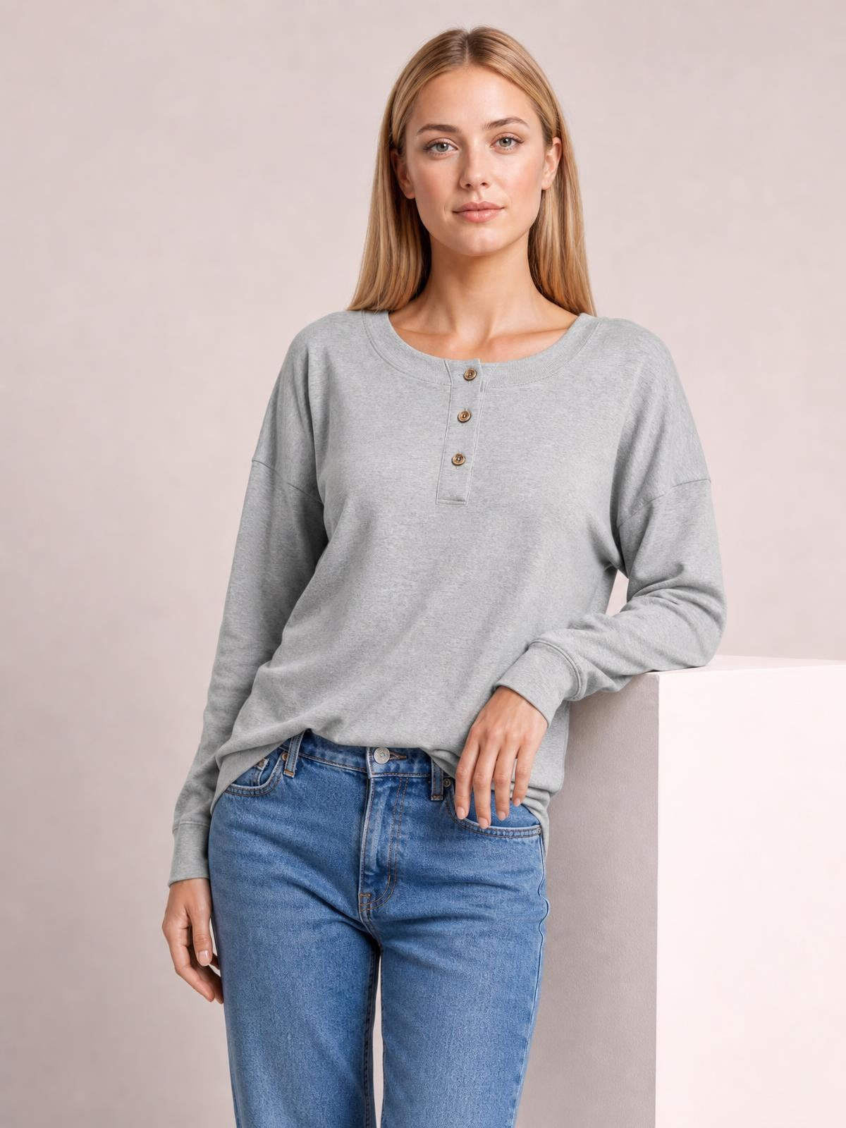 Model wearing a light gray quarter-button dropped-shoulder blouse with a relaxed silhouette, long sleeves, ribbed cuffs, and a round neckline.