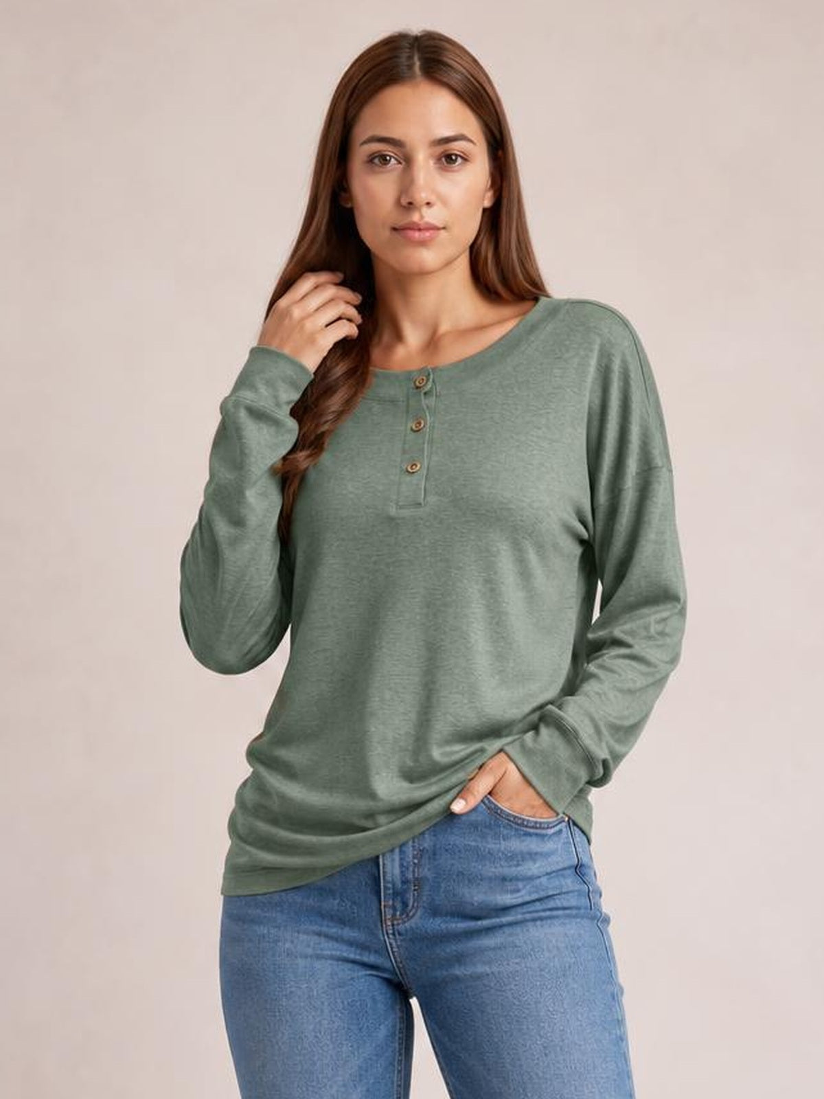 Model wearing a sage green quarter-button dropped-shoulder blouse with long sleeves and a relaxed, straight silhouette, posing with one hand in her jeans pocket.