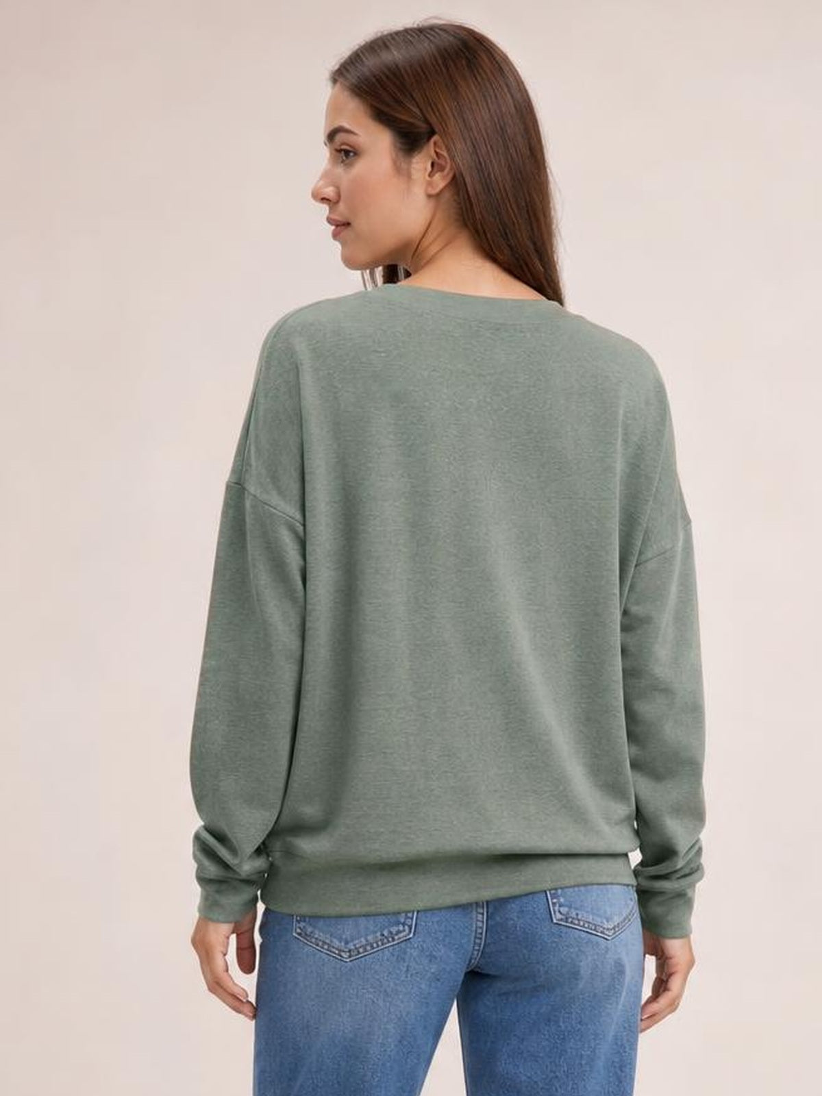 Model looks over her shoulder, showing the sage green dropped shoulder blouse from behind with a relaxed silhouette, long sleeves, ribbed cuffs, and hem.