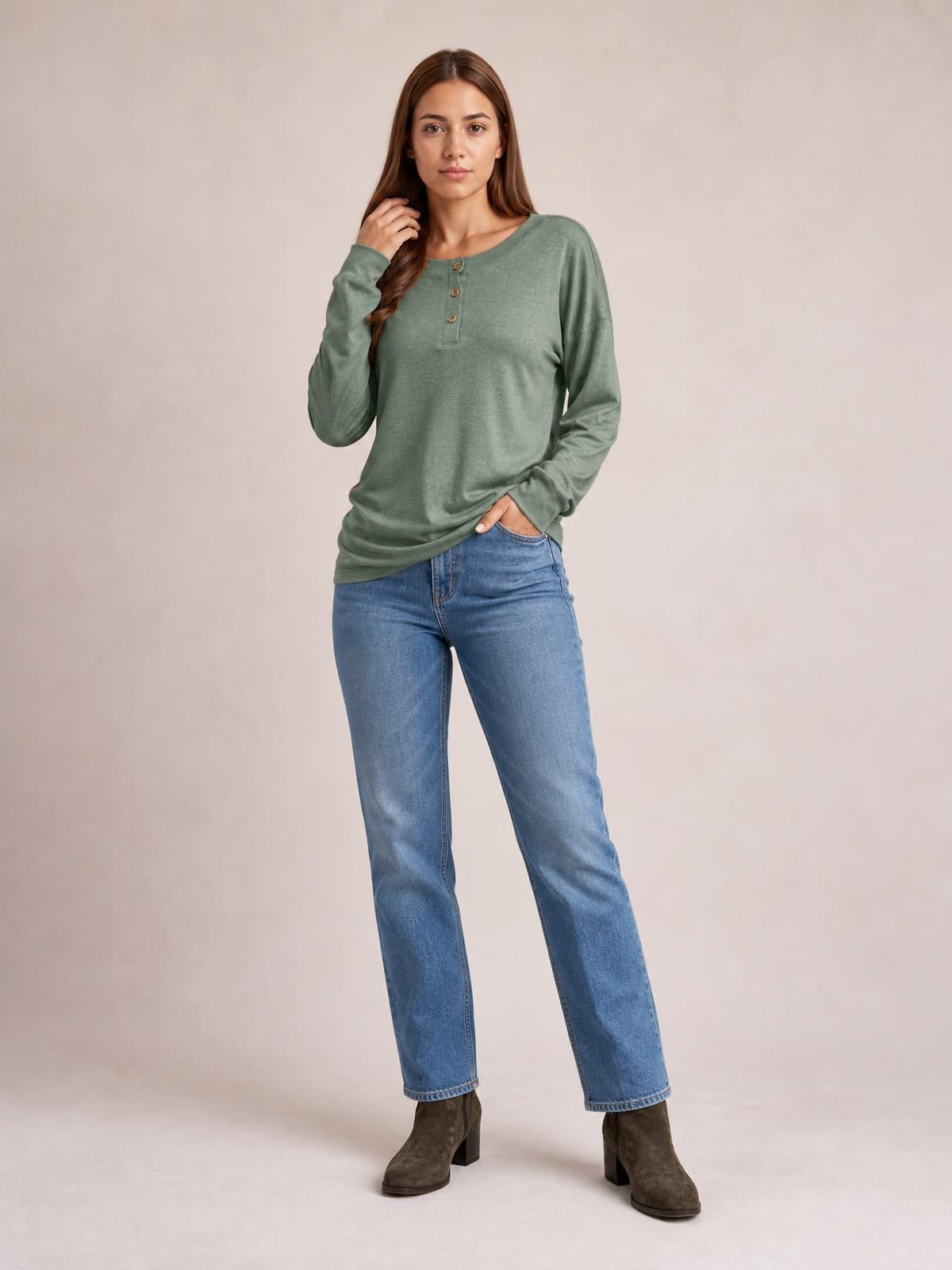 Model wears a sage green quarter-button dropped shoulder blouse with long sleeves and a relaxed silhouette, posing with one hand in her jeans pocket.