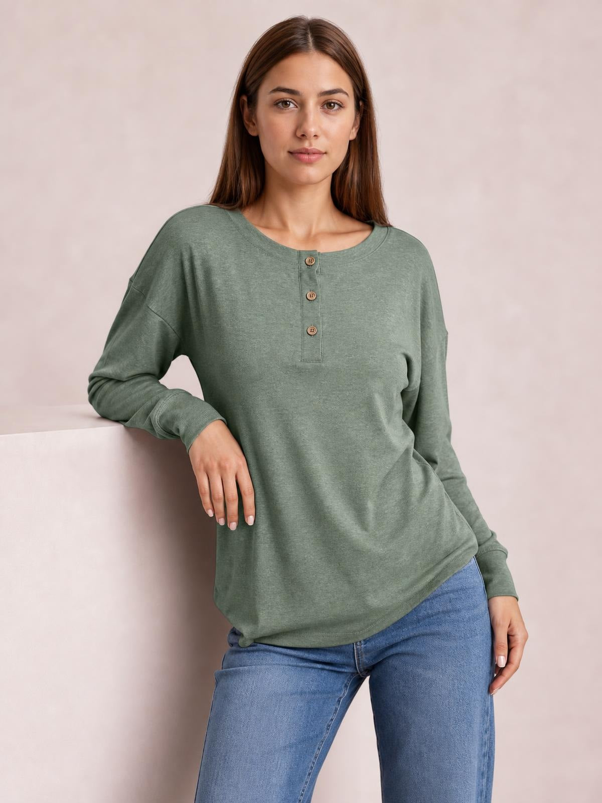 Model wears a sage green quarter-button blouse with a dropped-shoulder design, relaxed straight silhouette, rounded neckline, long sleeves, and a curved hem.