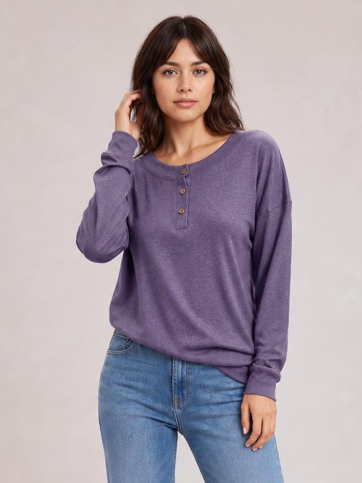 Model wearing a purple quarter button dropped shoulder blouse with a relaxed silhouette, long sleeves, ribbed cuffs, and a rounded neckline.