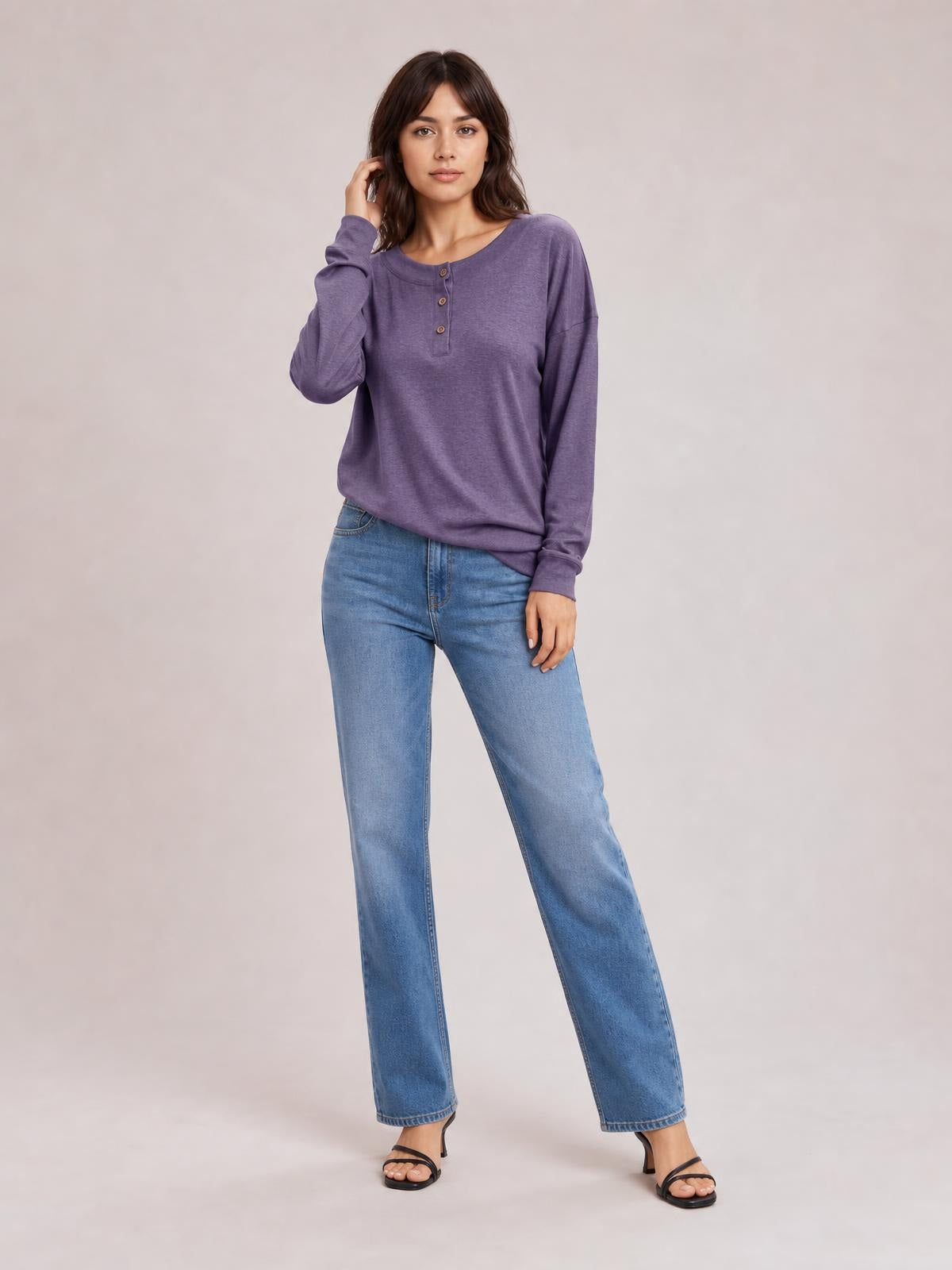 A woman models a purple quarter-button dropped-shoulder blouse with long sleeves and a relaxed silhouette, standing with one hand touching her hair.