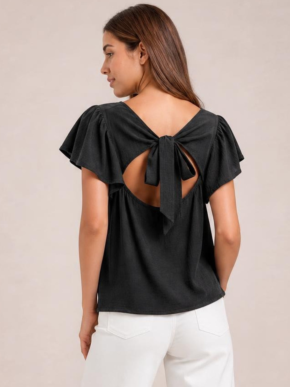 Model shown from the back in a solid black round-neck top with flutter sleeves, a regular silhouette, and a tie-back cutout with long bow tails.