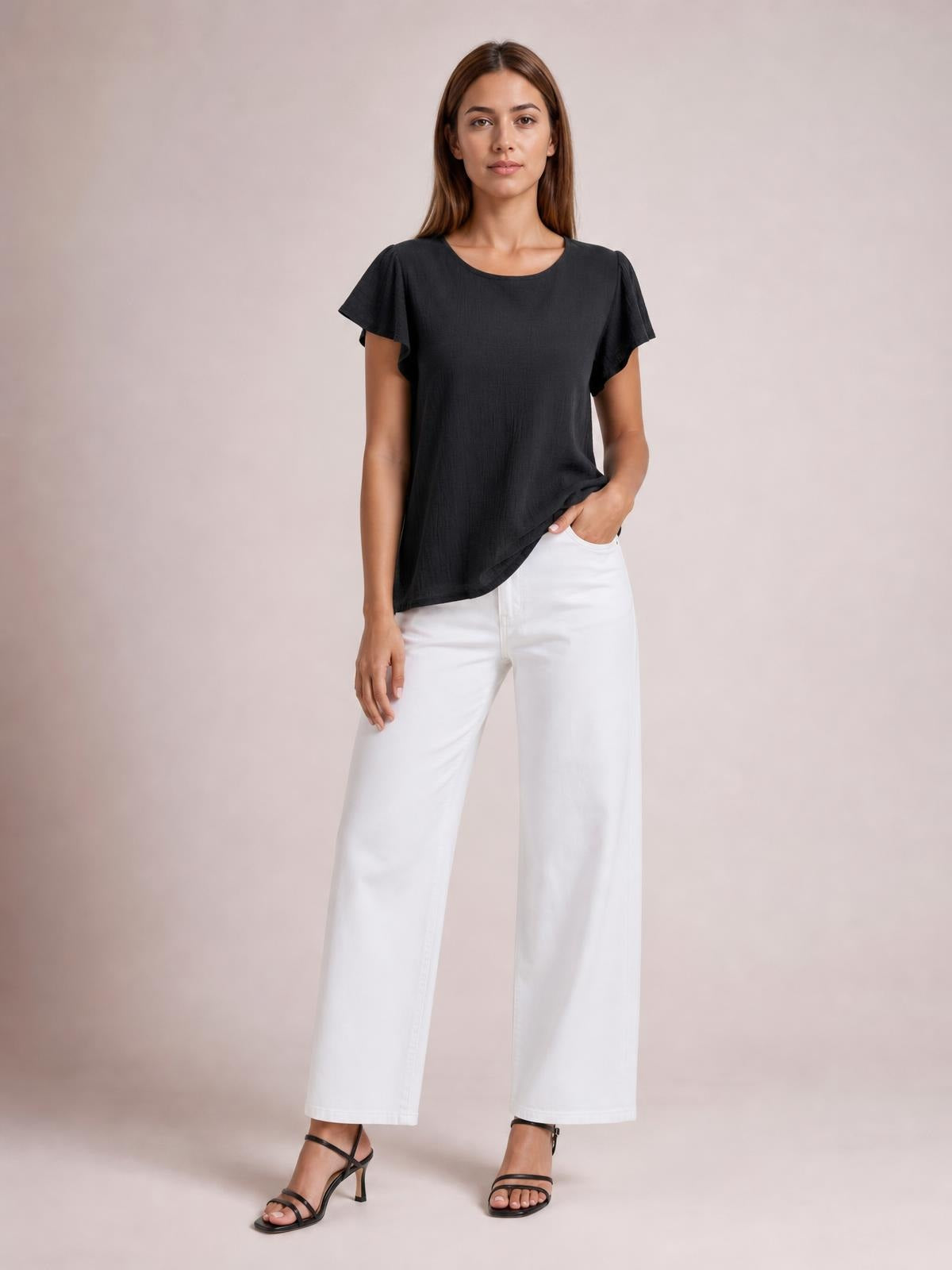 A model wears a solid black round-neck top with flutter short sleeves and a relaxed regular silhouette, lifting the hem slightly with one hand.