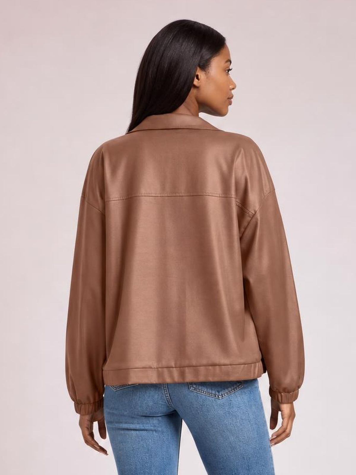 A model stands in a back view wearing a brown zip-up dropped shoulder jacket with a relaxed silhouette, long sleeves, elastic cuffs, and a seamed hem.