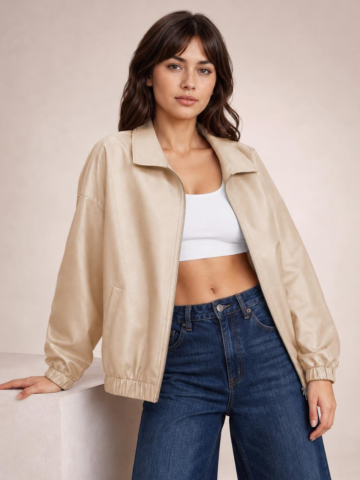 A model poses in a beige zip-up dropped shoulder jacket with a relaxed silhouette, wide collar, long sleeves, elastic cuffs and hem, and visible front pockets.
