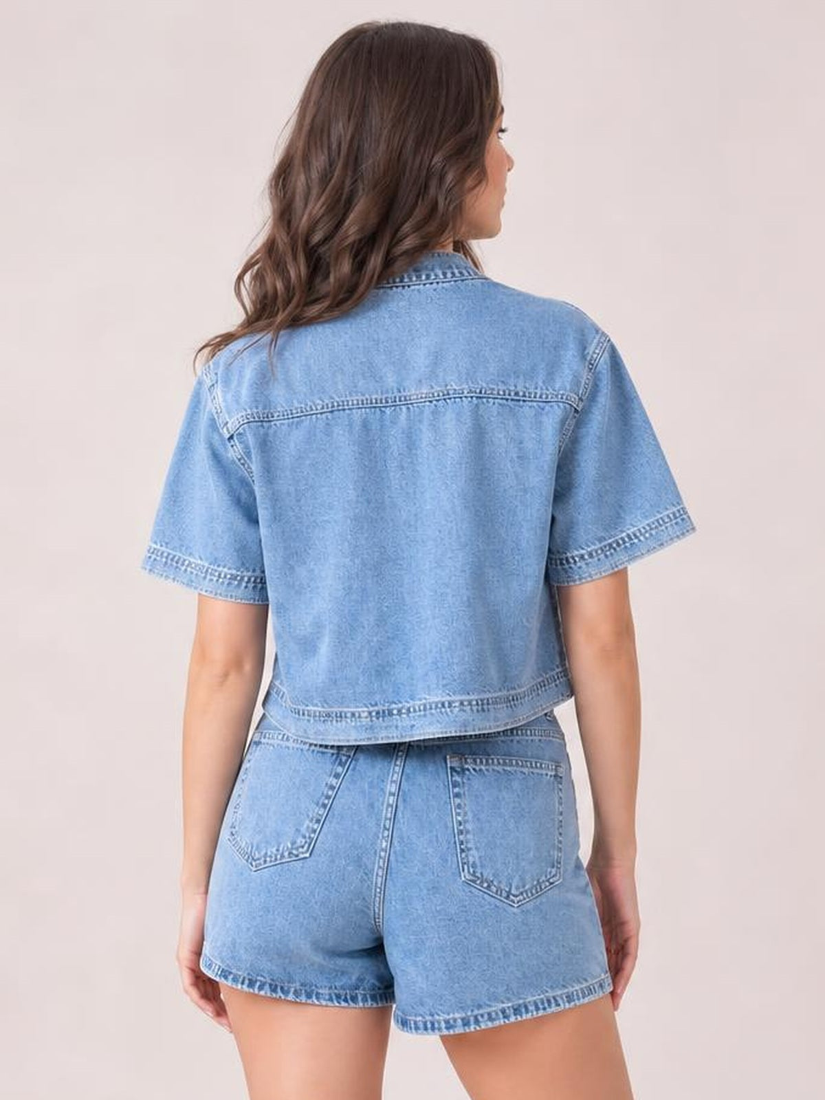 Model shown from behind wearing a light blue denim short-sleeve top with a cropped silhouette and matching high-waisted skort with back pockets.