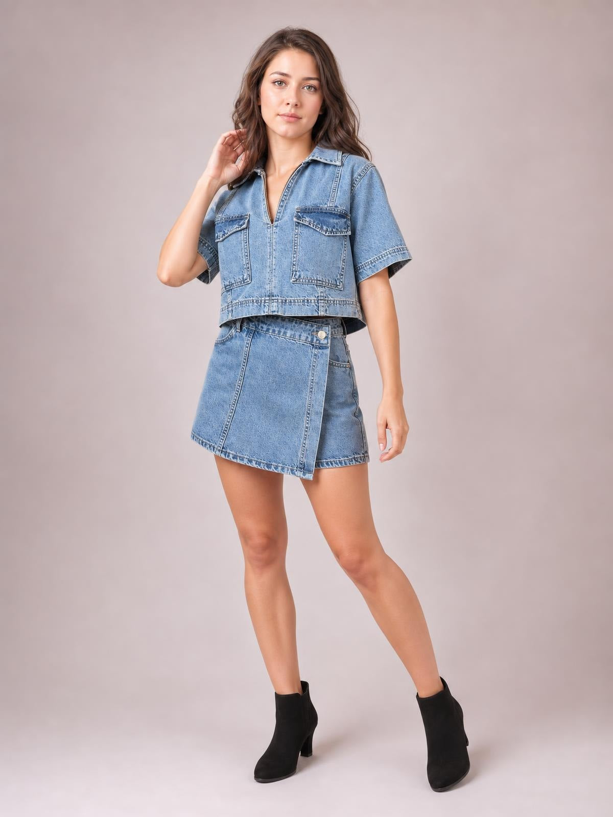 A model poses in a light blue denim set with a short-sleeve Johnny collar top, buttoned chest pockets, and an asymmetrical skort silhouette.