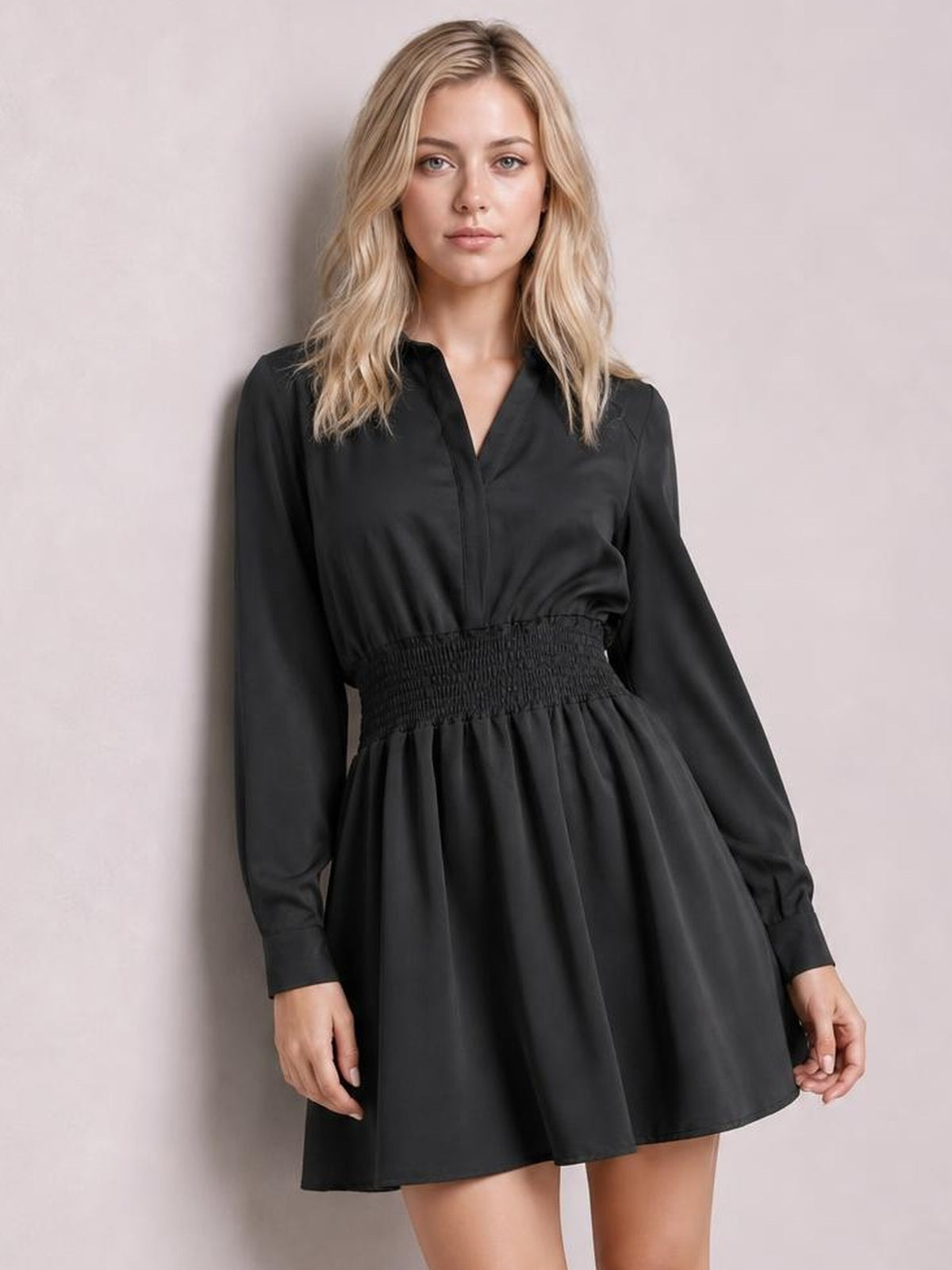 A model stands facing forward in a black Johnny collar mini dress with long sleeves, a smocked waist, and a softly flared skirt silhouette.