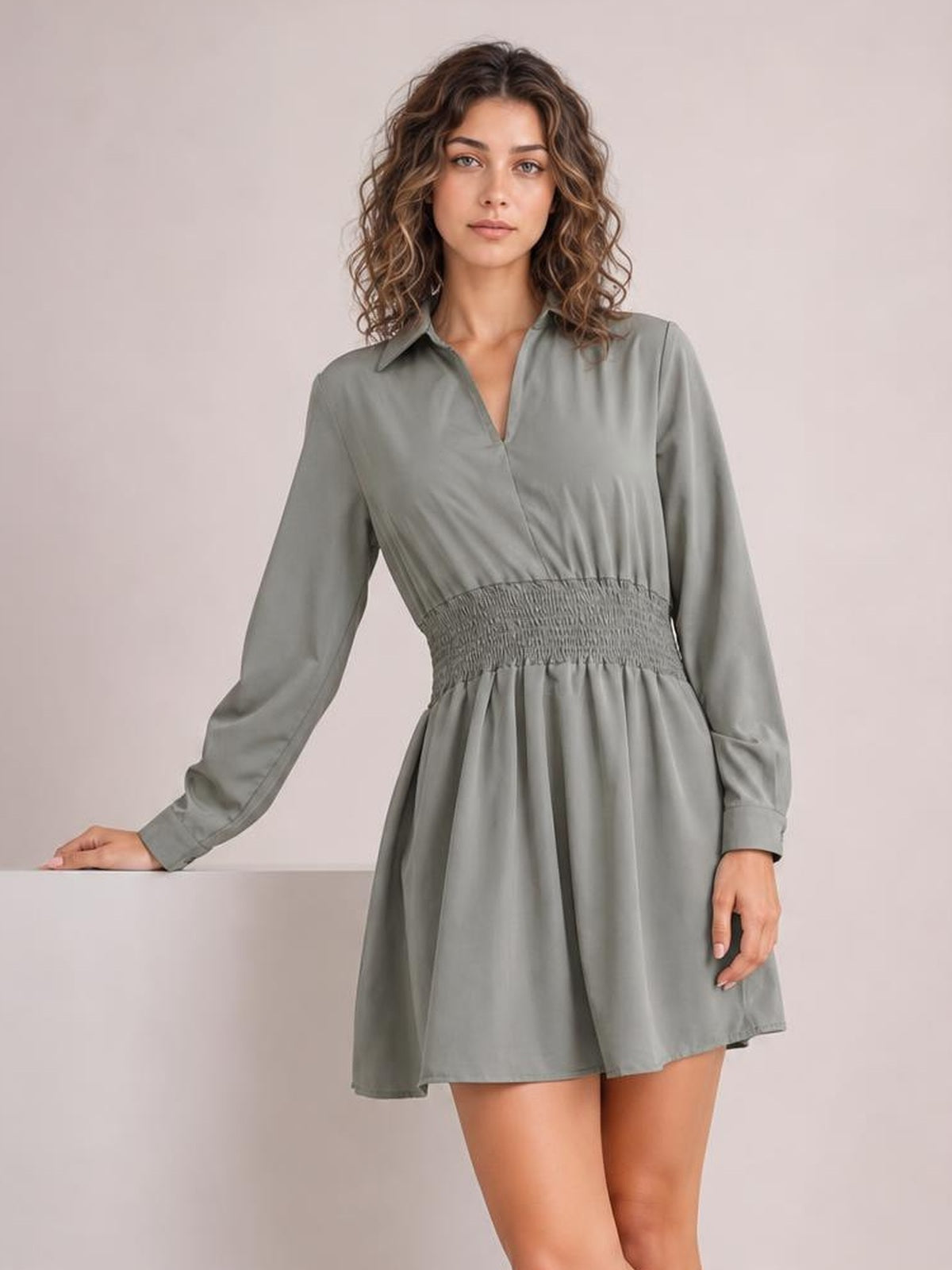 A model poses in a gray Johnny collar mini dress with long sleeves, a V-neck opening, smocked waist, and a softly flared skirt silhouette.