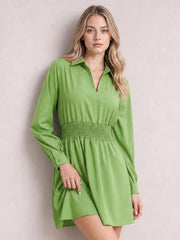 Model poses in a lime green Johnny collar mini dress with long sleeves, a smocked waist, relaxed silhouette, button cuffs, and a gently flared skirt.