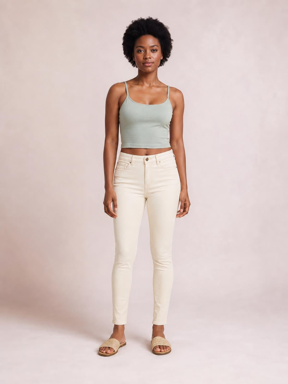 A model stands facing forward in light cream, high-rise tummy control skinny jeans with a sleek skinny silhouette, belt loops, pockets, and button closure.