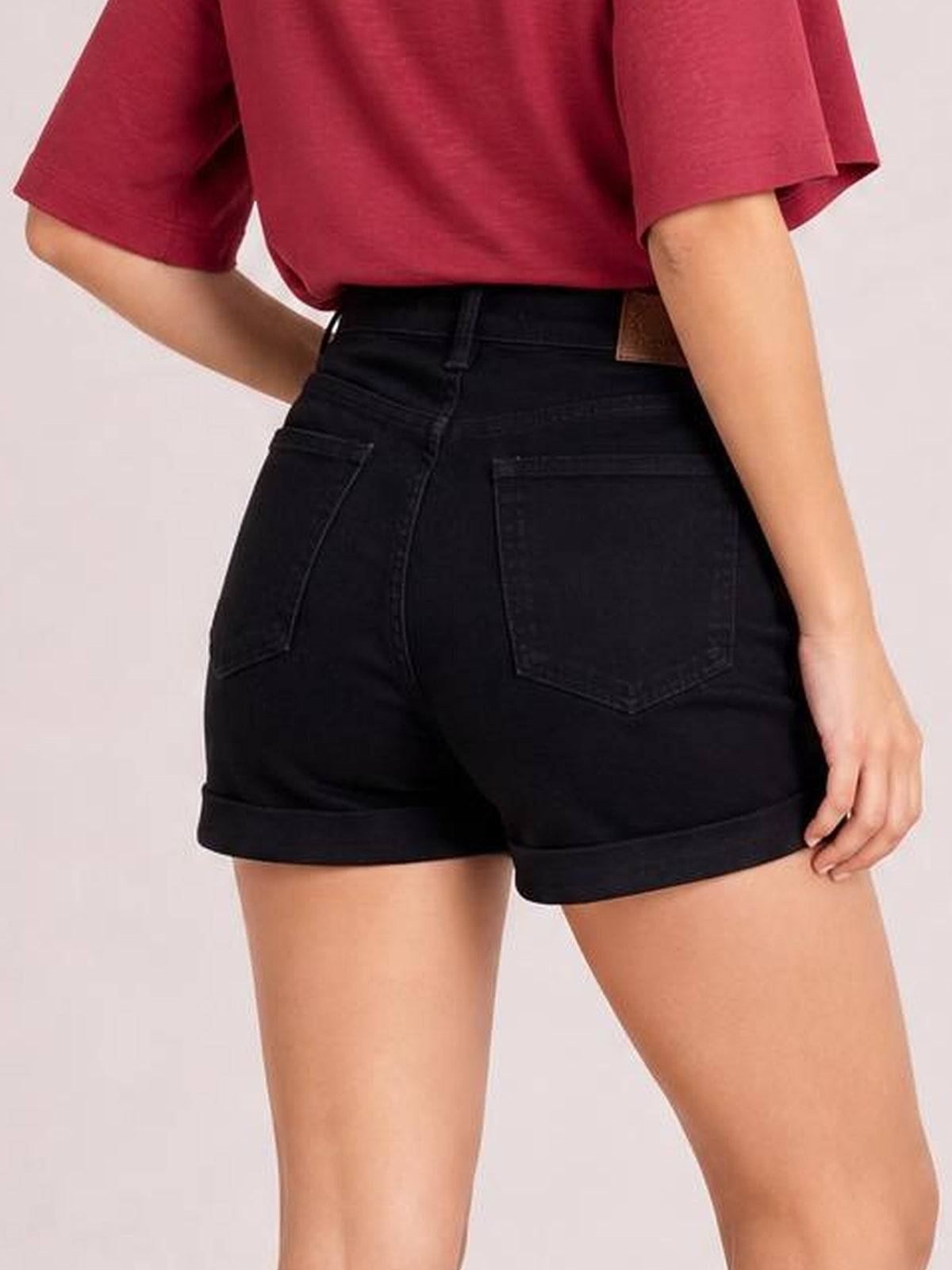 Model poses with one hand on her hip, showcasing black high-waist tummy control denim shorts with a fitted silhouette, back pockets, and cuffed hems.