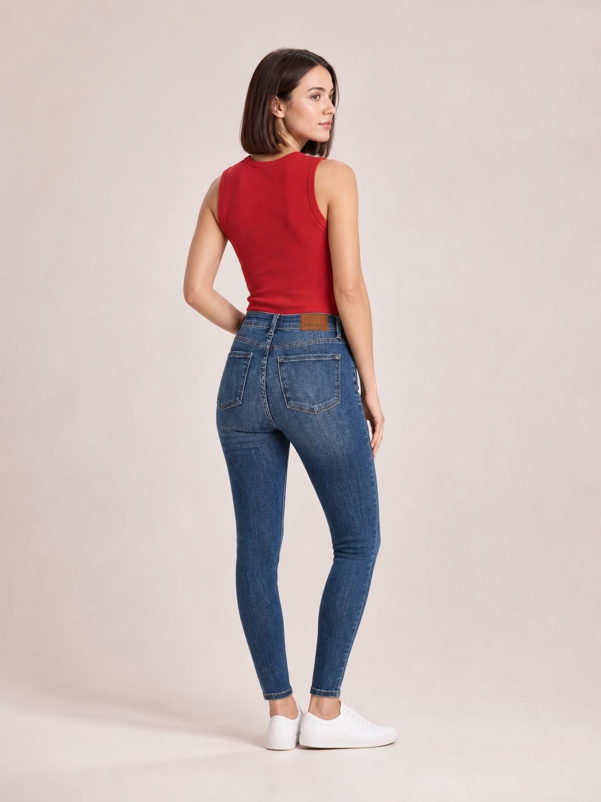 A model poses from the back in blue JuBlue mid-waist distressed slim jeans with a fitted silhouette, belt loops, waistband, and two patch pockets.