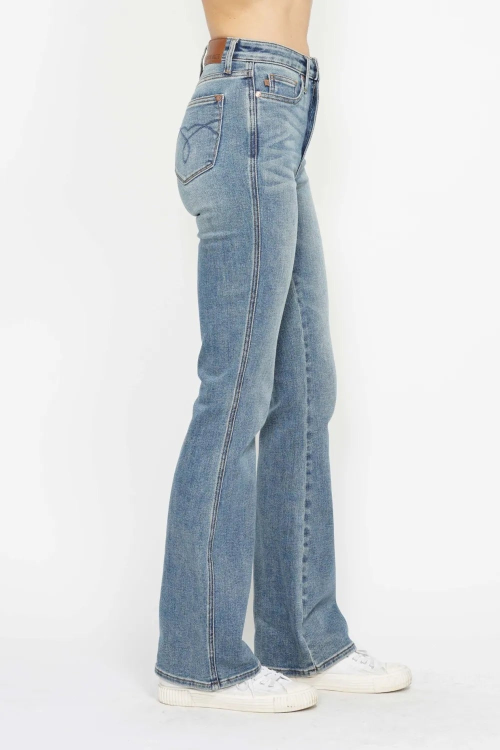Model shown in profile wearing light-wash tummy control bootcut jeans with back embroidered pockets, belt loops, zip fly, and a stretchy fitted-to-flared silhouette.