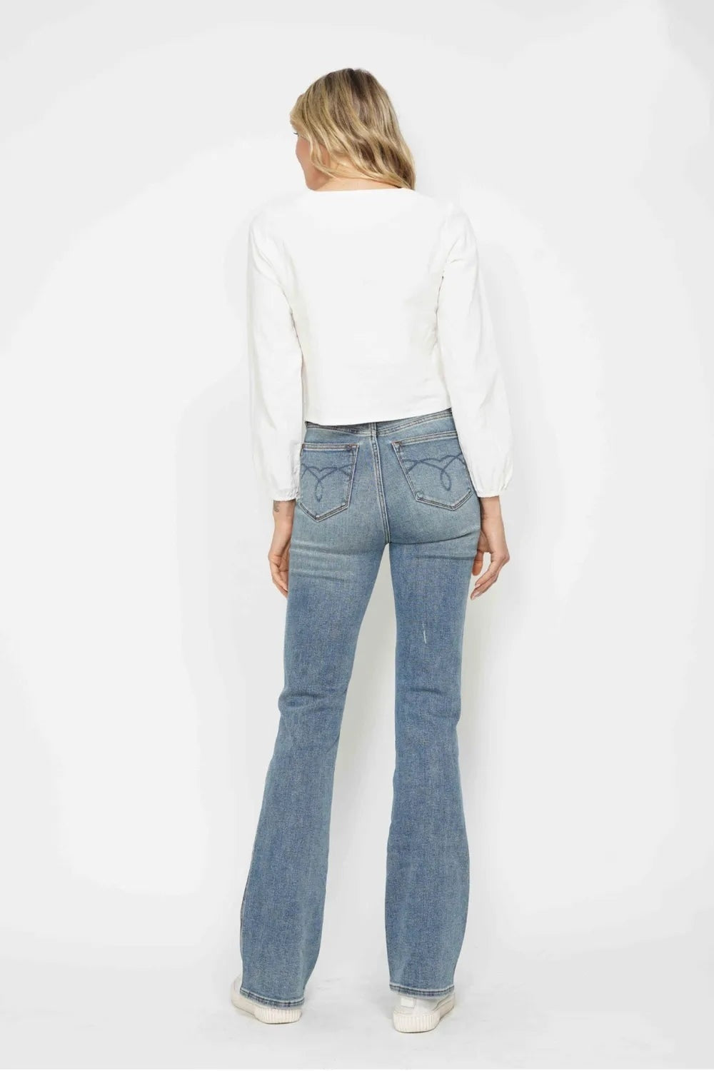 Model shown from the back wearing light-wash tummy control bootcut jeans with embroidered back pockets, a high-rise waist, fitted legs, and flared hems.