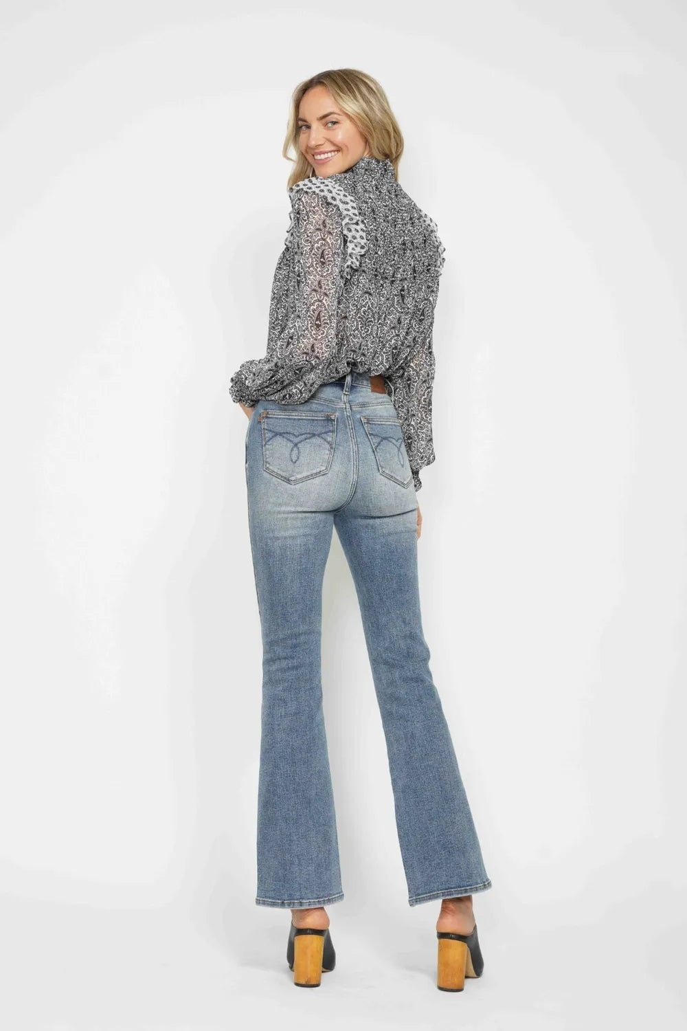 A model turns to show light-wash tummy-control jeans with embroidered back pockets, a fitted high-rise silhouette, and flared bootcut legs.
