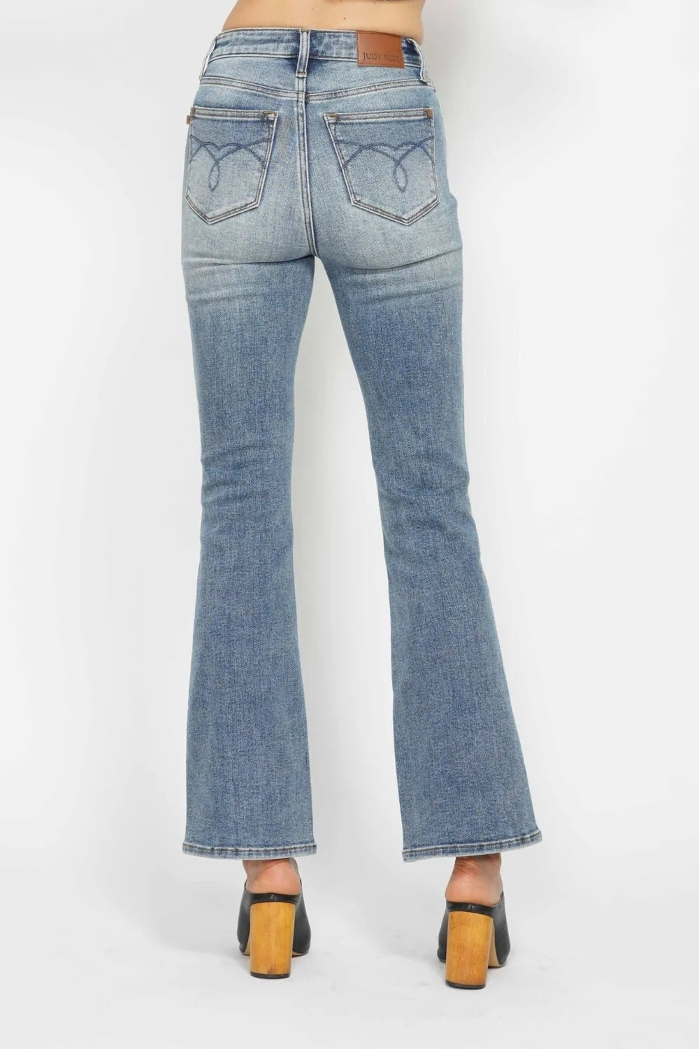 Model shown from behind wearing light blue tummy control bootcut jeans with belt loops, back embroidered pockets, a fitted hip, and flared hems.