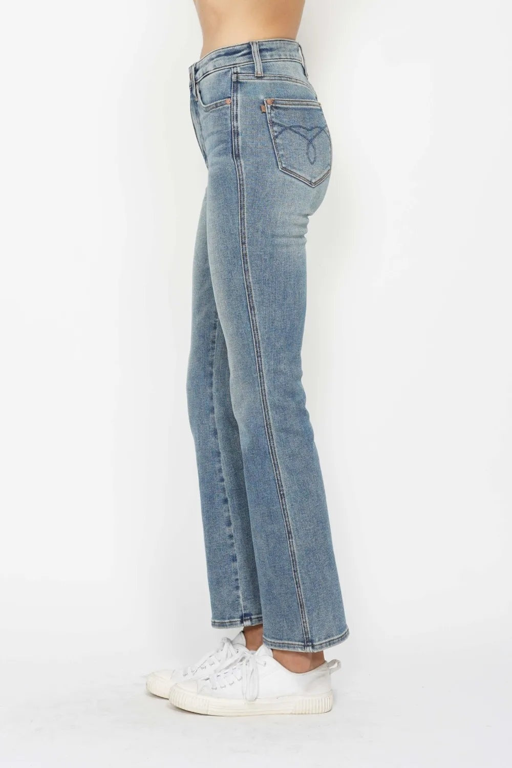 Model stands in a side-back pose wearing light-wash tummy control bootcut jeans with a contoured waistband, belt loops, and embroidered back pockets.