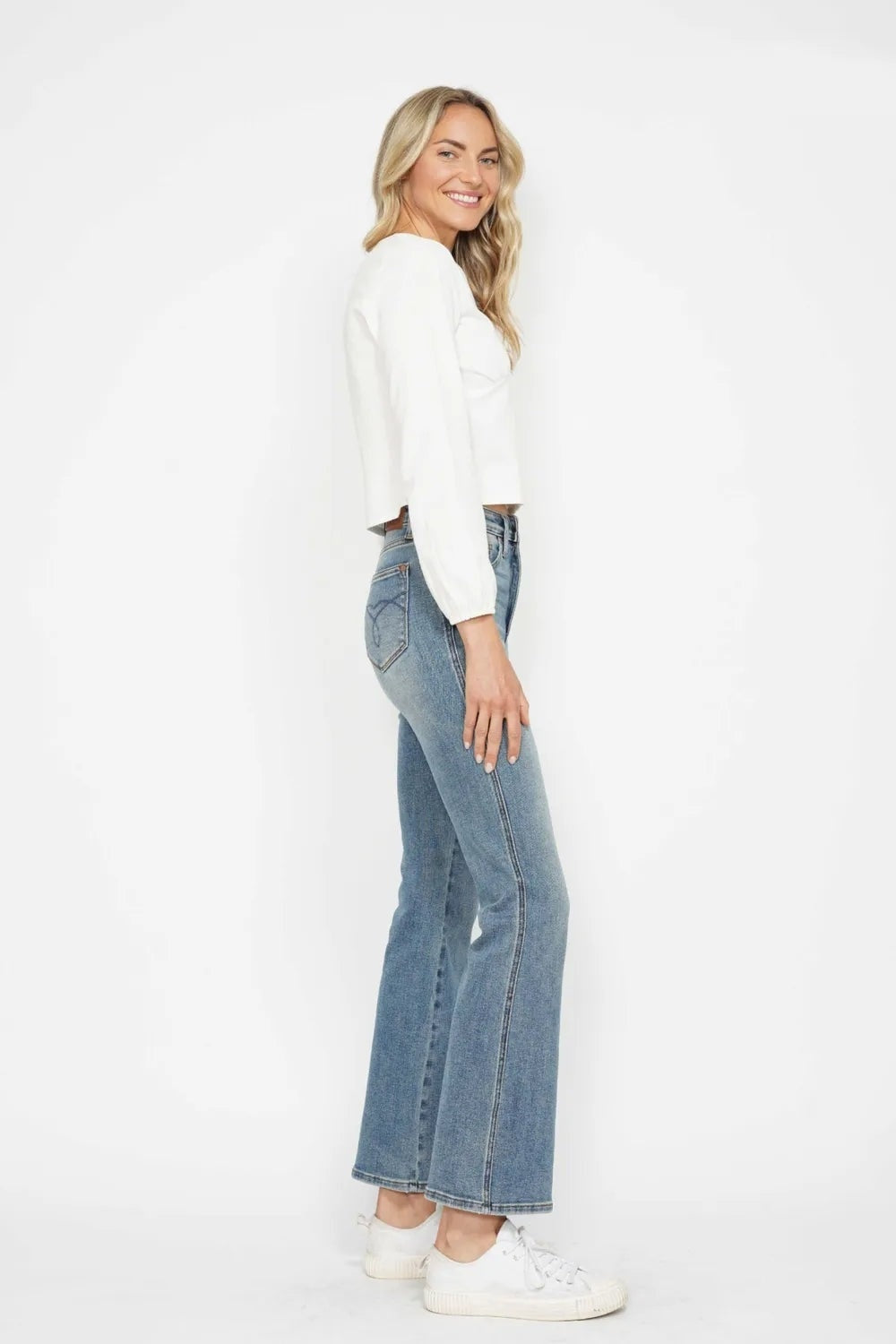 A model poses in light-wash tummy control jeans with an embroidered back pocket, fitted hips, and a relaxed bootcut silhouette.