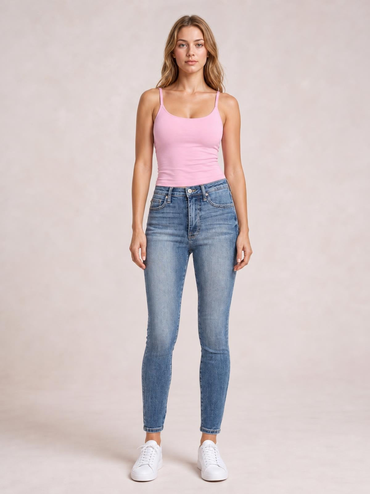 Model standing front-facing in high-rise blue skinny jeans with a light contrast wash, tummy control waistband, classic pockets, and fitted ankle-length legs.