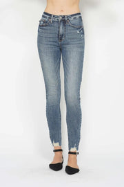 Model stands facing forward in blue vintage-wash tummy control skinny jeans with front pockets, belt loops, stretch fit, and distressed raw hems.