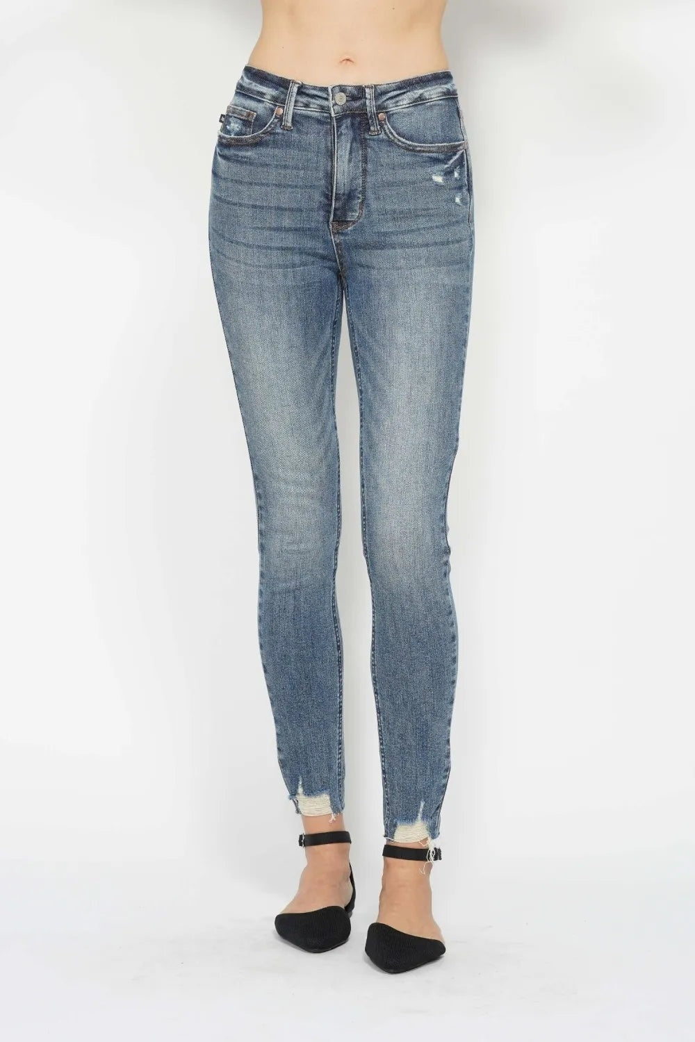 Model stands facing forward in blue vintage-wash tummy control skinny jeans with front pockets, belt loops, stretch fit, and distressed raw hems.