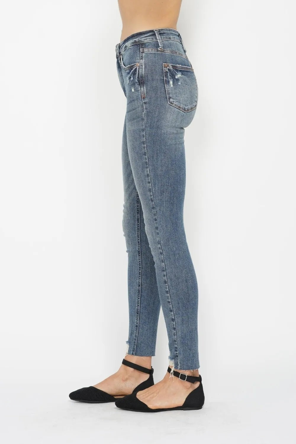 Model shown in profile wearing blue vintage wash tummy control skinny jeans with back pockets, a fitted silhouette, and distressed frayed hems.