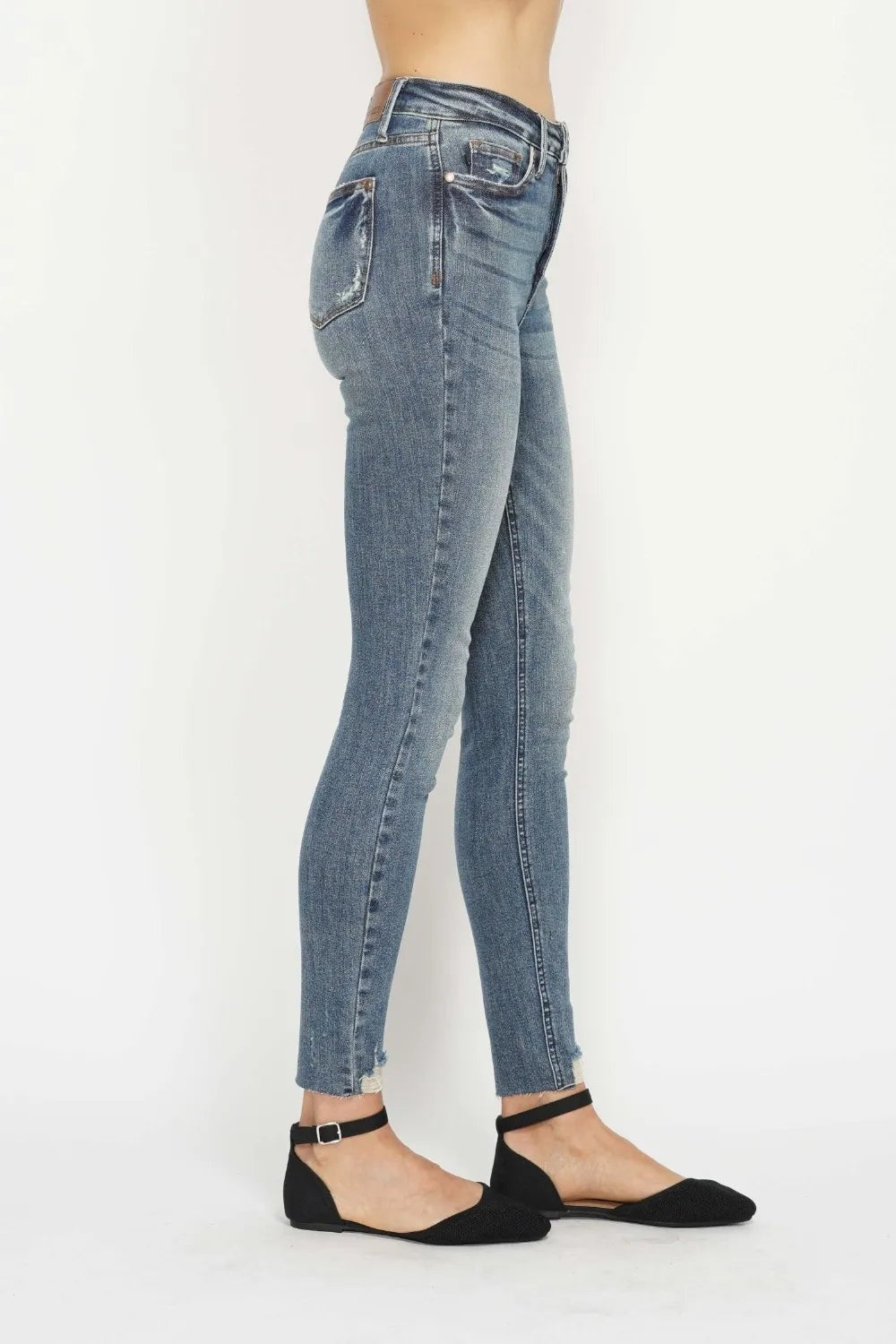 Model in a side pose wears light vintage-wash skinny jeans with a fitted silhouette, five-pocket construction, tummy-control waistband, and distressed raw hems.