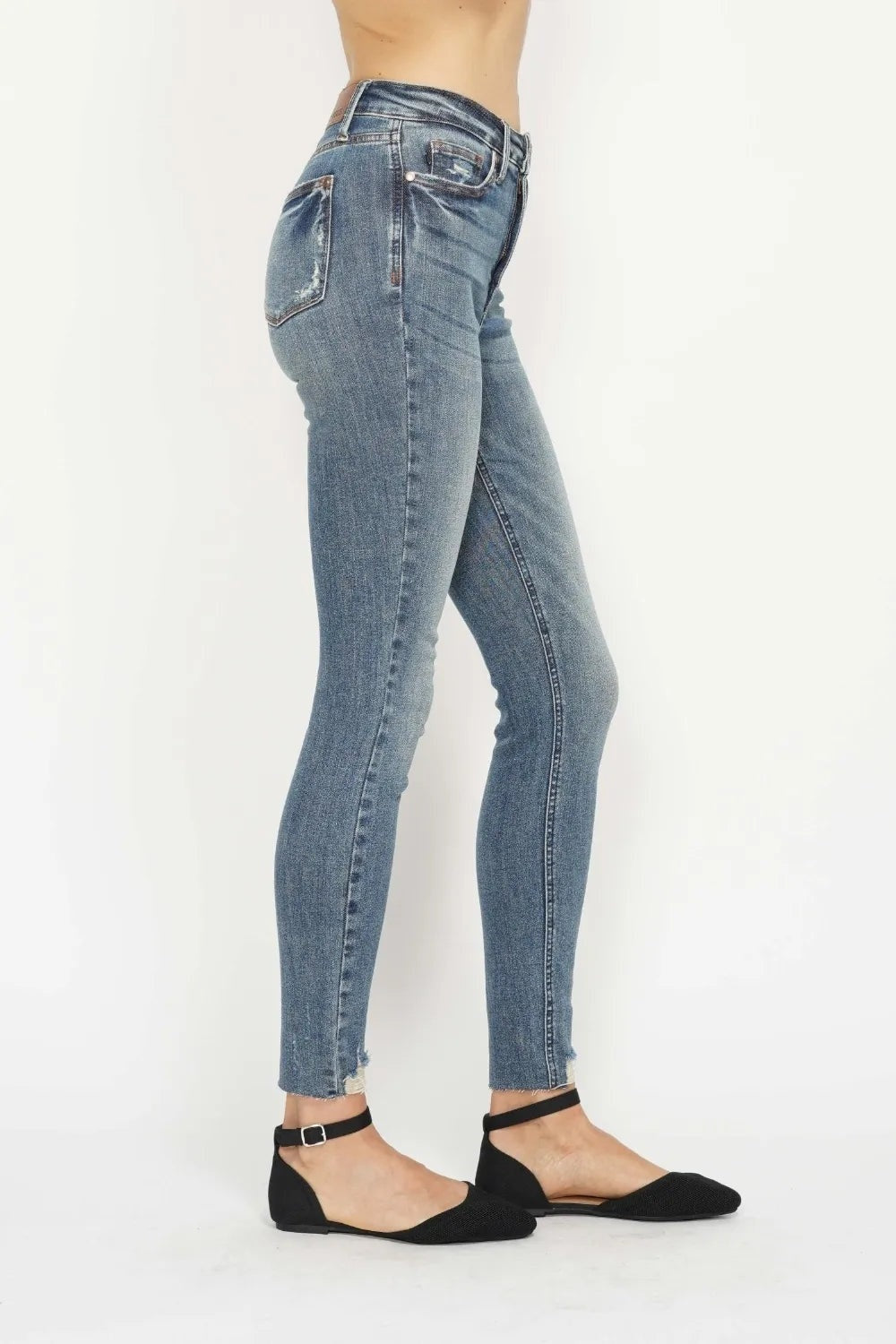 A cropped model poses in light-blue vintage-wash tummy-control skinny jeans with back pockets, moderate stretch, and distressed frayed hems.
