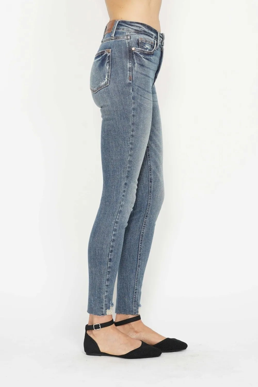 A side-view model wears blue vintage-wash tummy-control skinny jeans with back pockets, a fitted silhouette, and frayed distressed hems.