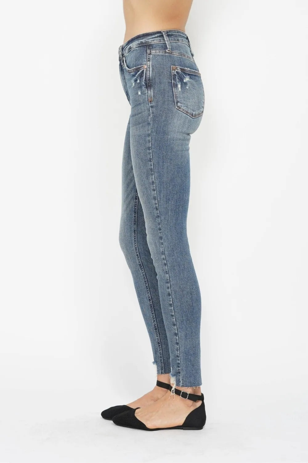 Model shown in side profile wears light-blue vintage-wash tummy control skinny jeans with back pockets, belt loops, moderate stretch, and distressed hems.