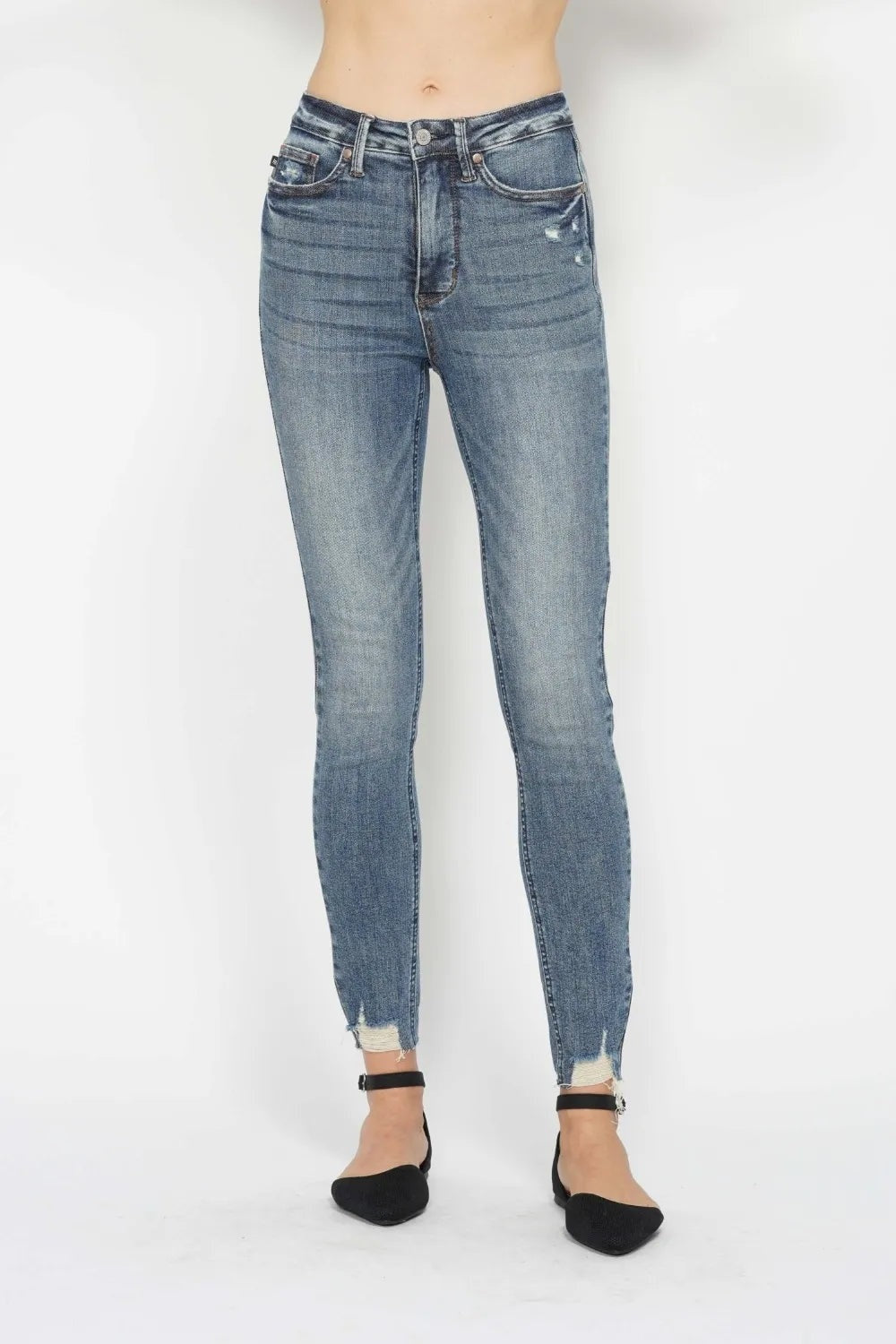 Model stands front-facing in vintage-wash tummy control skinny jeans with a high-rise waistband, five-pocket construction, and frayed distressed hems.