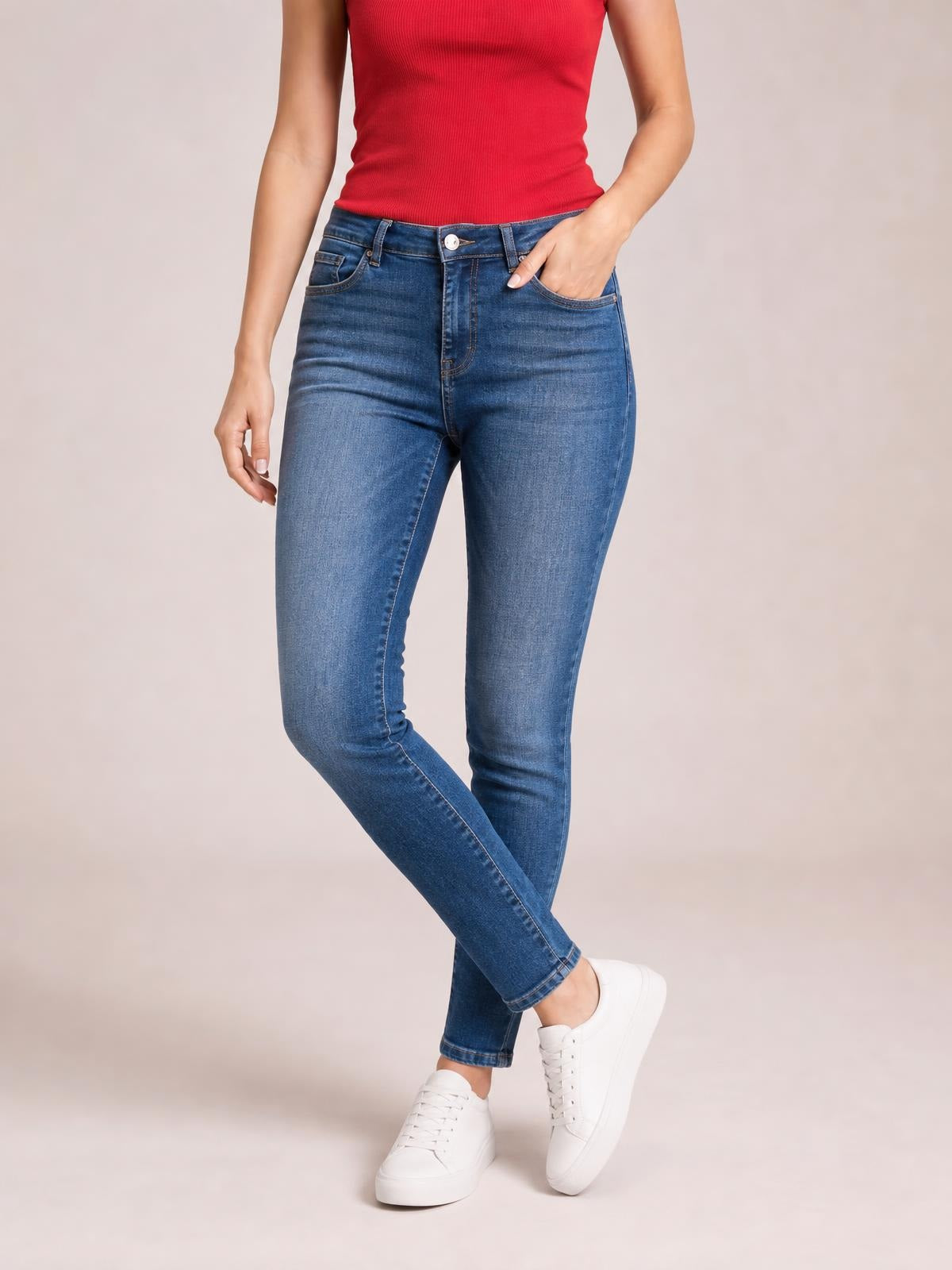 Model wearing blue washed thermal skinny jeans with a button closure, pockets, and fitted silhouette, posed with one hand in a pocket and crossed legs.