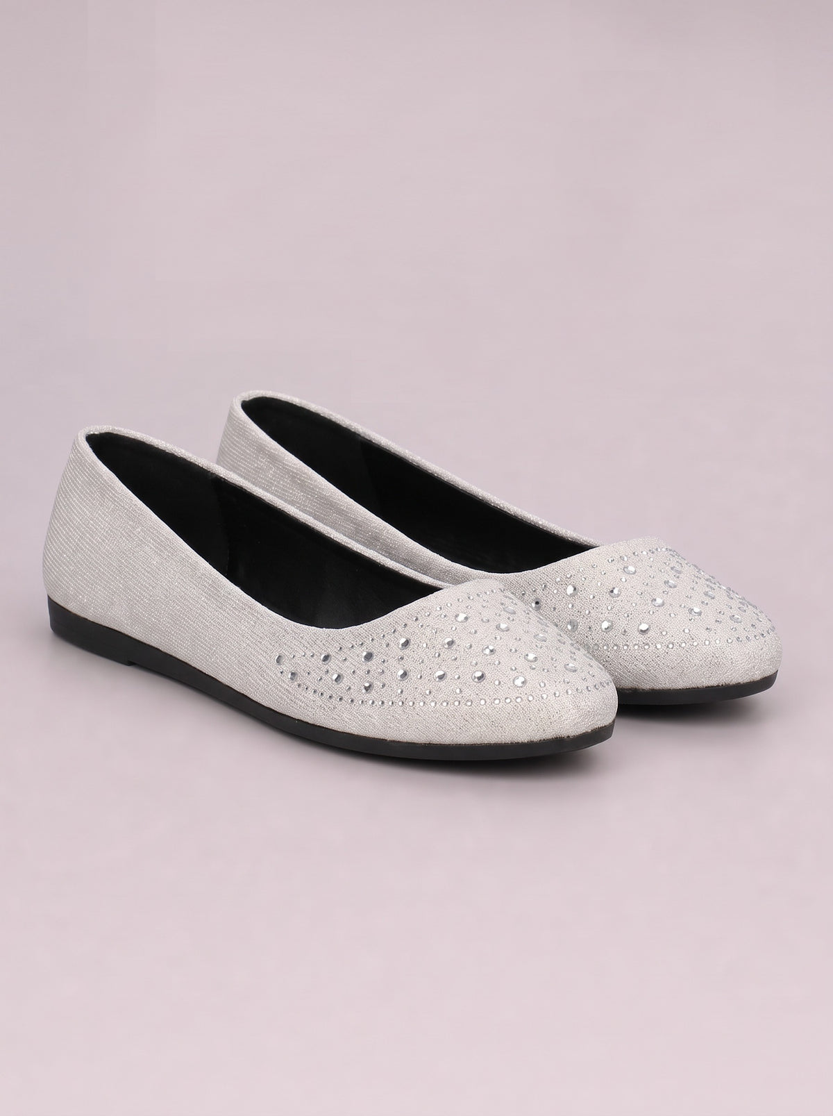 White rhinestone flat slip-ons with rounded toes, glittering embellished uppers, black interiors, and low black rubber soles.