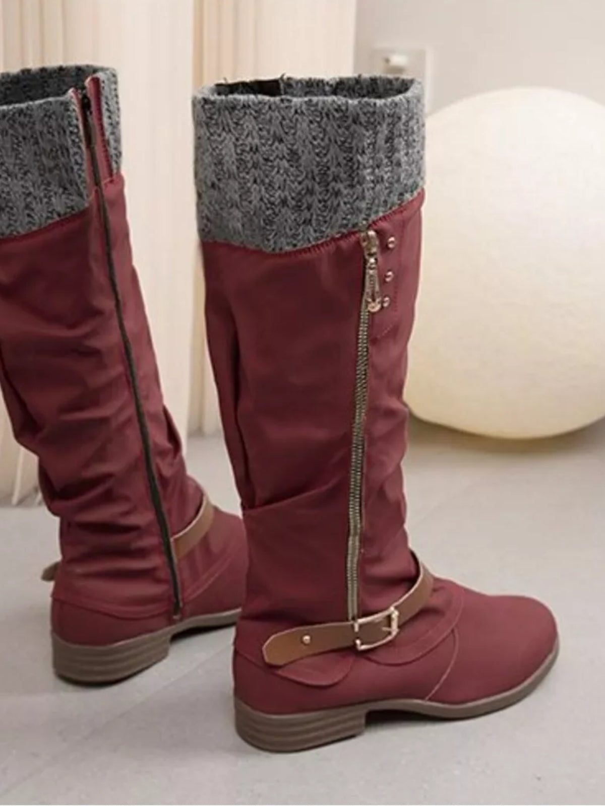 Burgundy knee-high slouch boots feature gray knit cuffs, low stacked heels, side zippers, buckled ankle straps, and textured rubber soles.