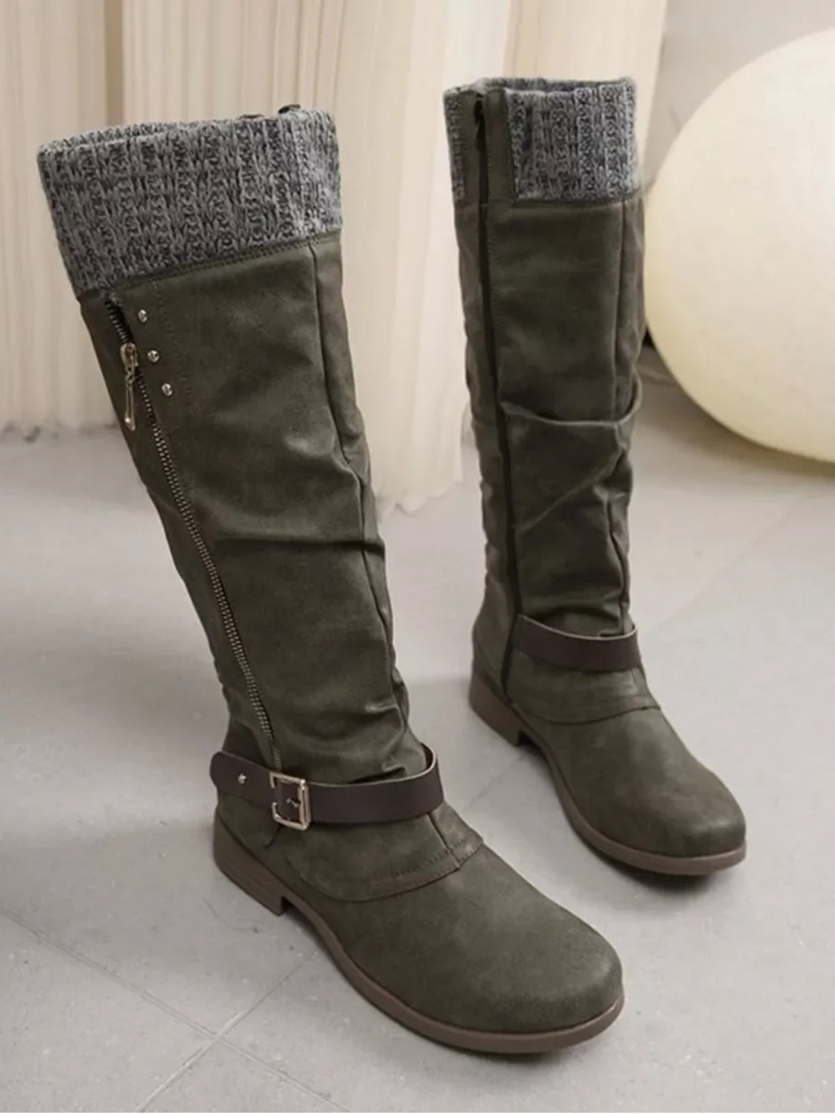 Olive-gray suede knee-high slouch boots feature cozy knit cuffs, side zippers, buckle ankle straps, rounded toes, and low rubber heels.