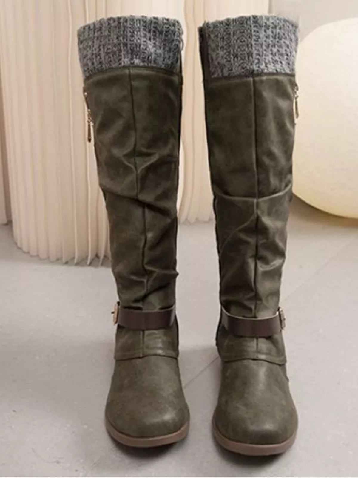 Olive-gray suede knee-high slouch boots feature cozy gray knit cuffs, low heels, rounded toes, side zippers, and buckle straps around the ankles.