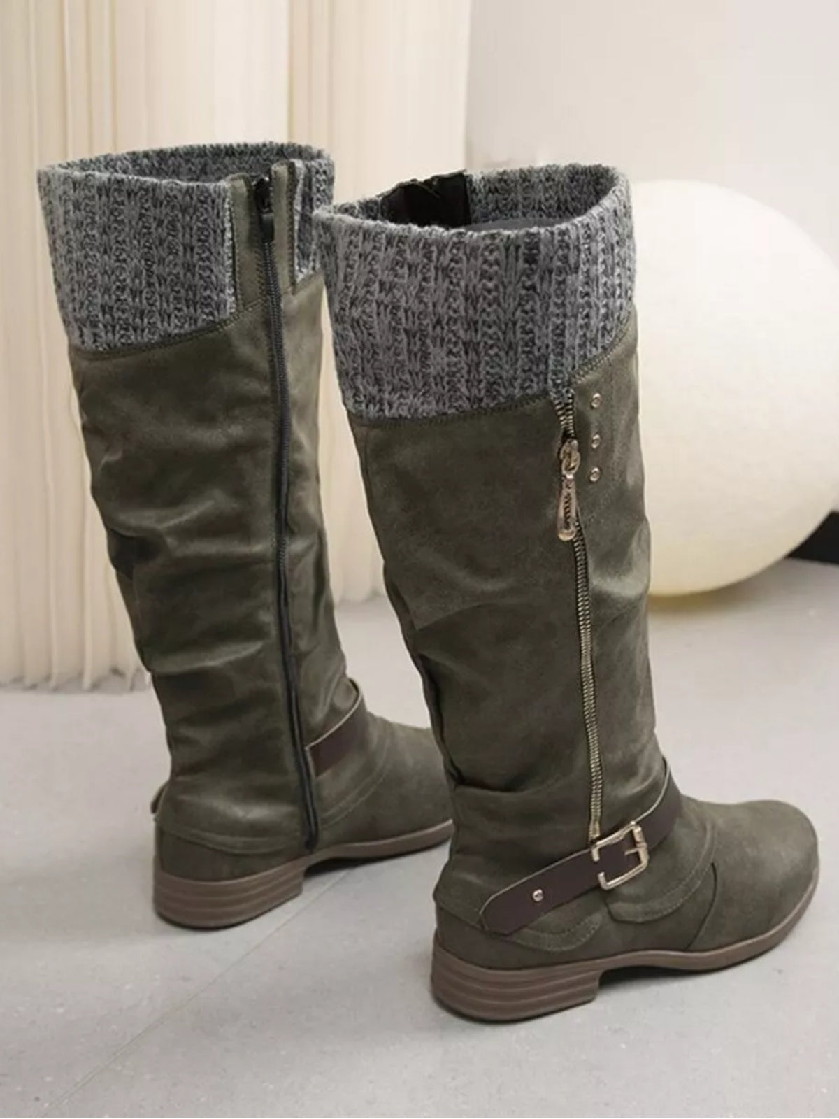 Olive green suede knee-high slouch boots feature cozy gray knit cuffs, side zippers, buckle ankle straps, rounded toes, and low stacked heels.